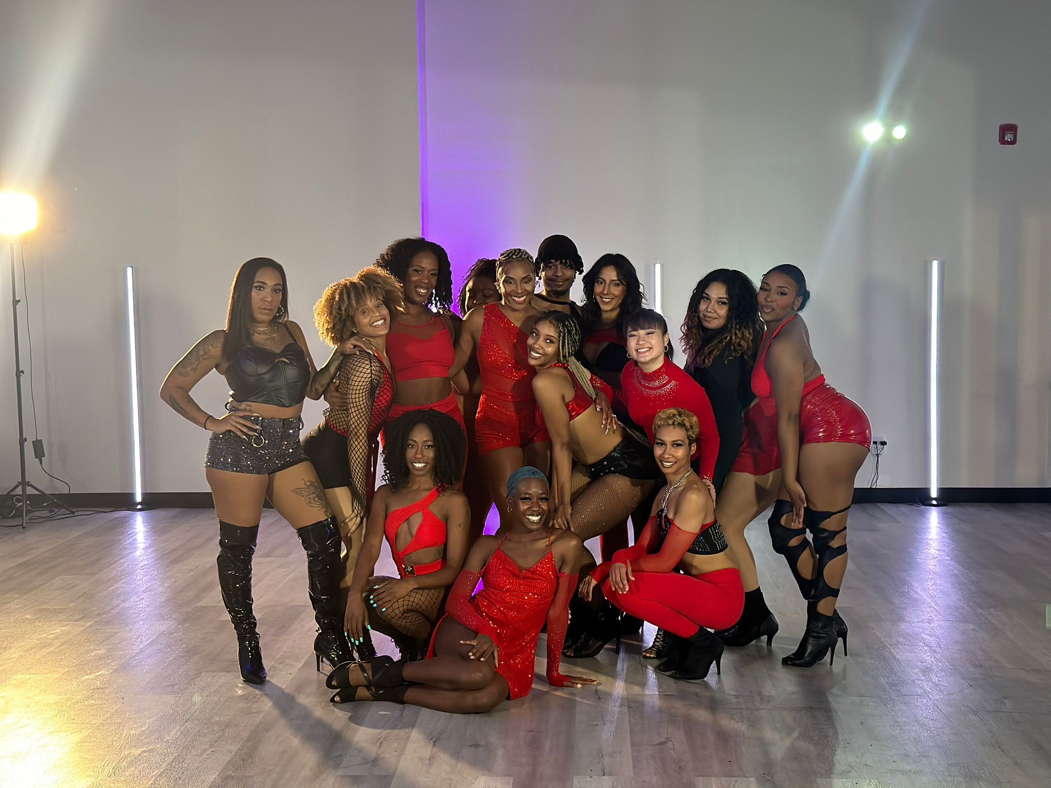 Group of women in dance costumes posing indoors with a plain wall background.