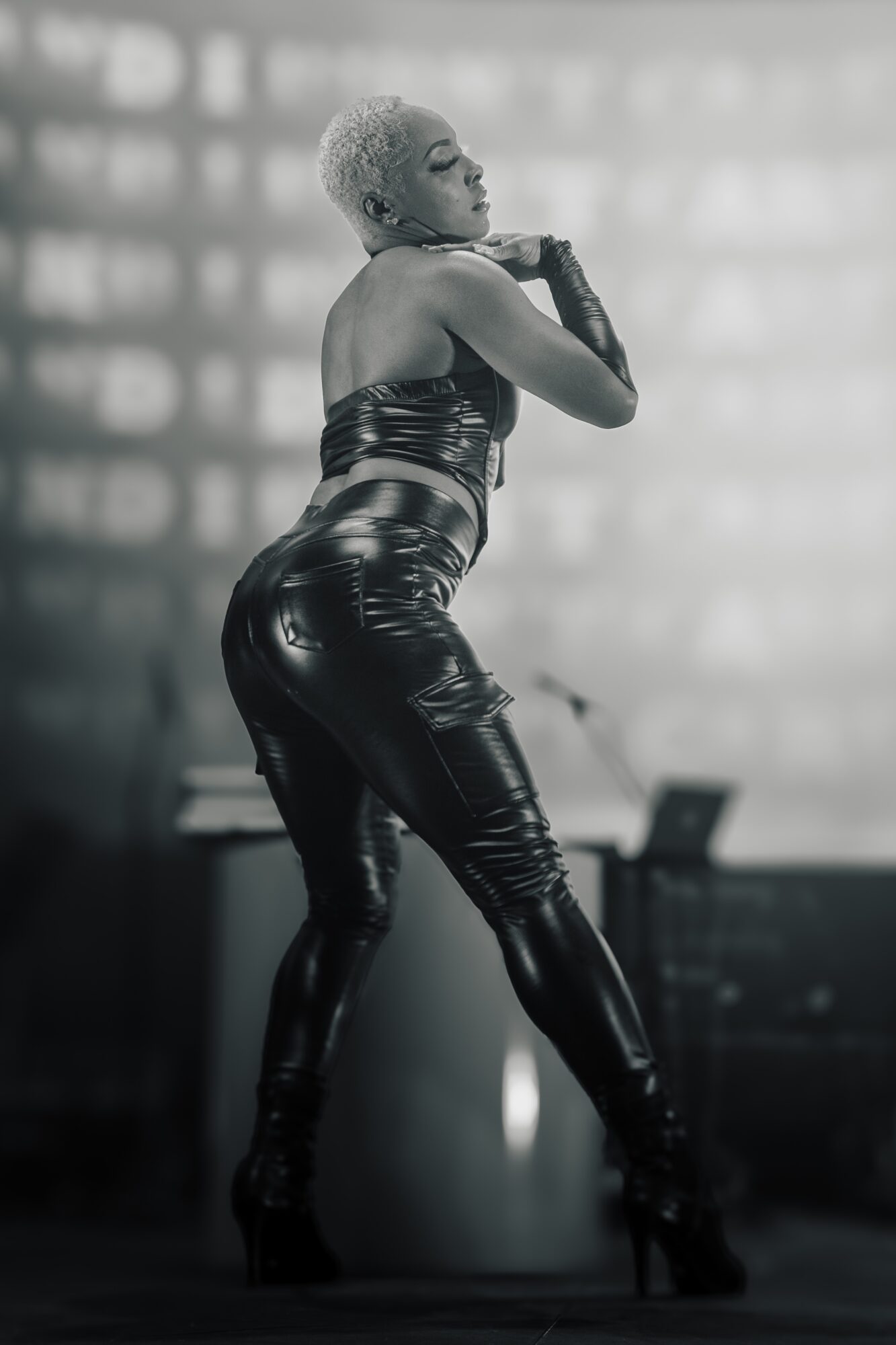 Woman with short hair in a shiny outfit poses on stage with a blurred background.