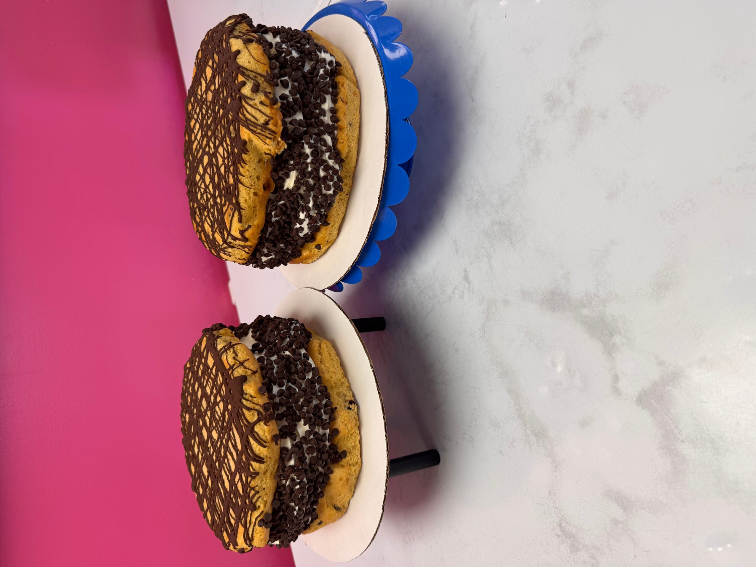 Two decorated cakes on white plates with black stands, against a pink and white background.