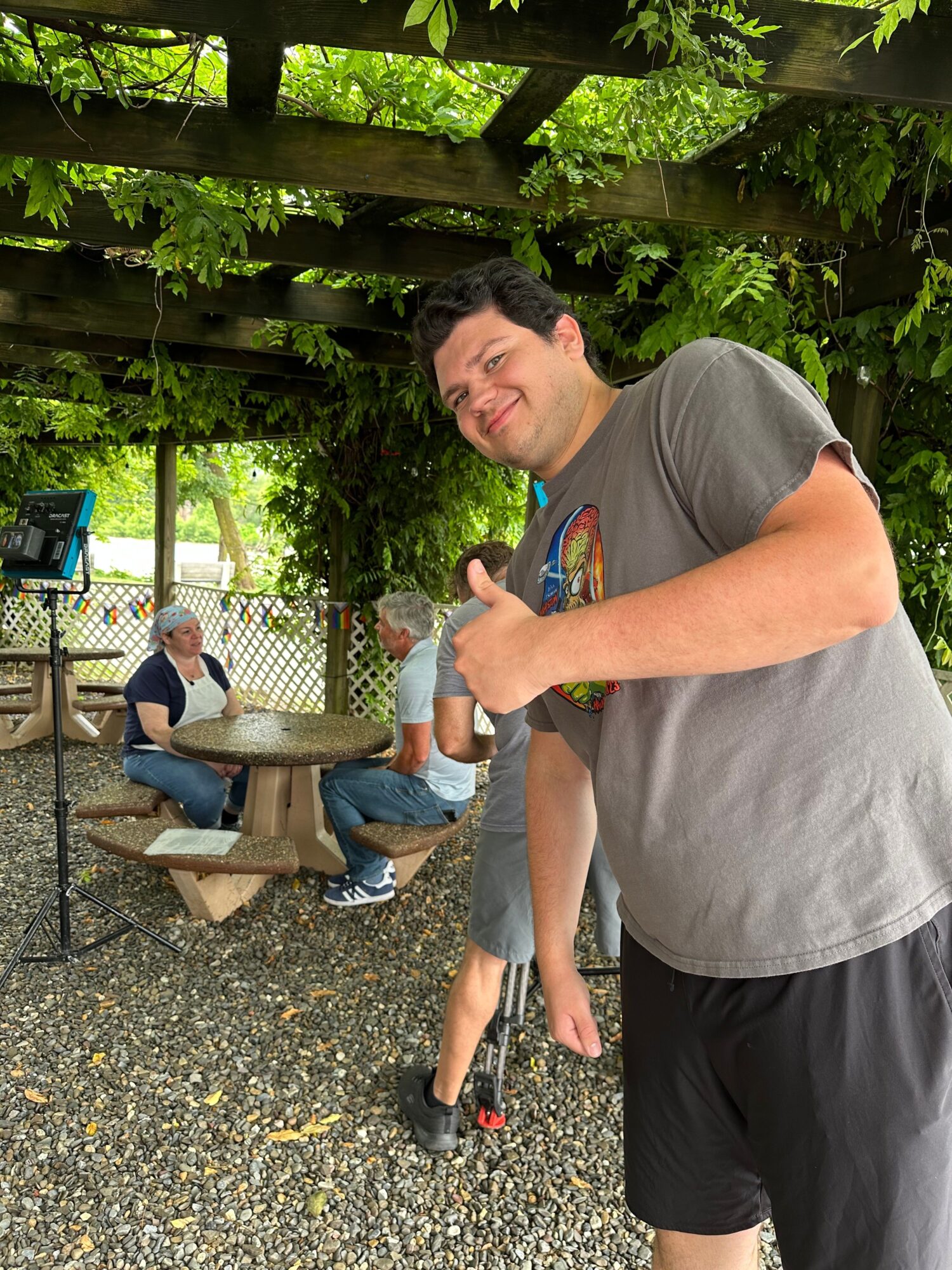 Person holding a water bottle outdoors, with a person sitting on a bench in the background, surrounded by greenery.