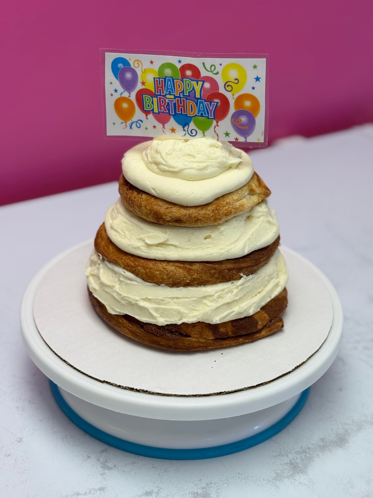 Three cream-filled cookies stacked on a white plate with a birthday card in the background, pink wall behind.