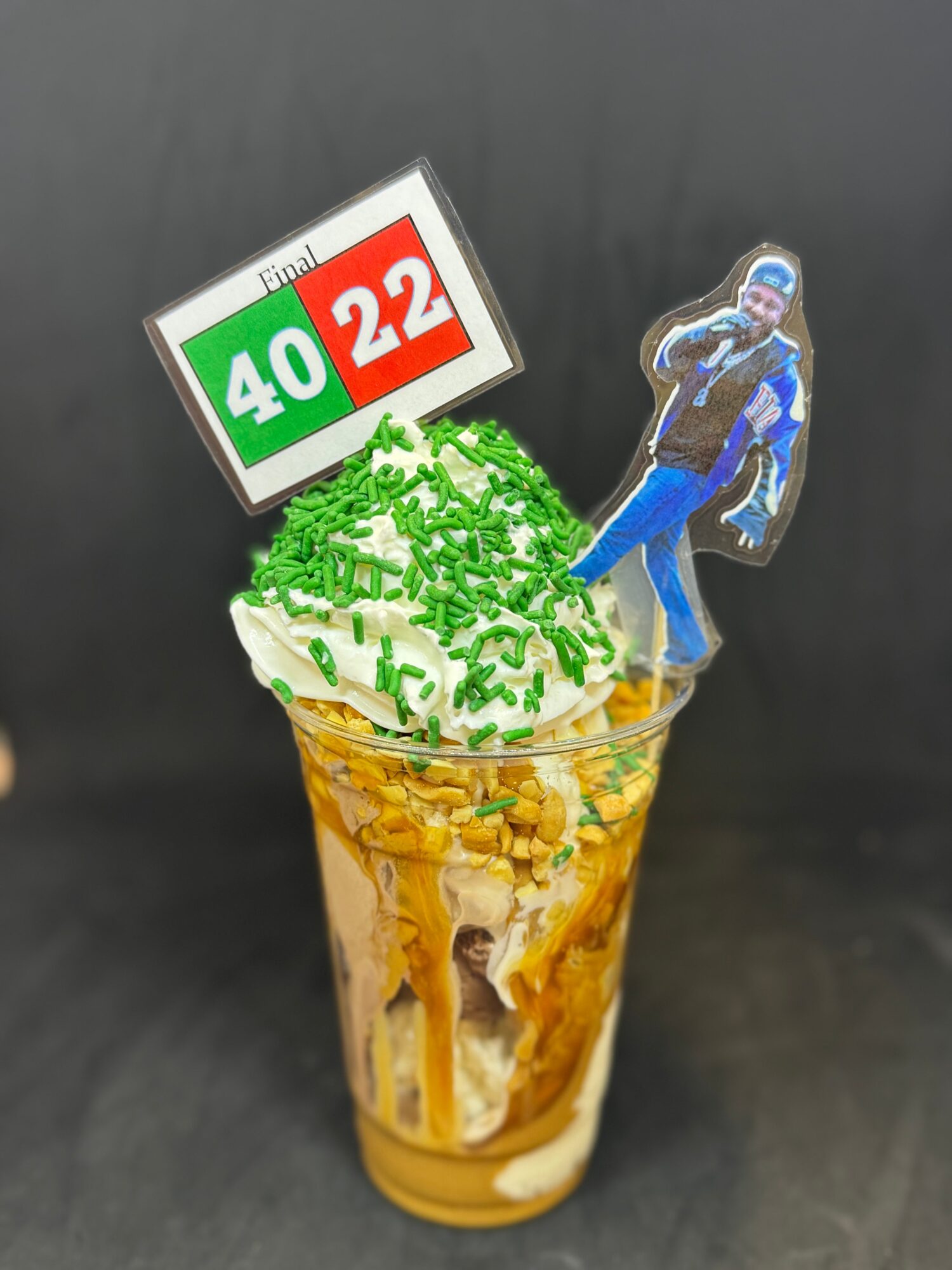 Ice cream sundae with green sprinkles, a football-themed sign, and a football player cutout, in a clear cup against a dark background.