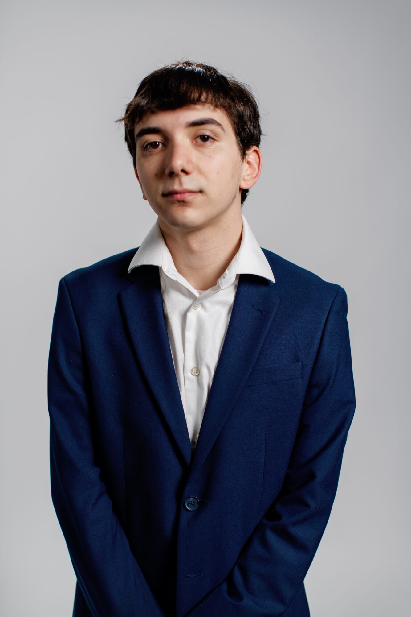 Young man in a blue suit and white shirt against a plain background, looking at the camera.