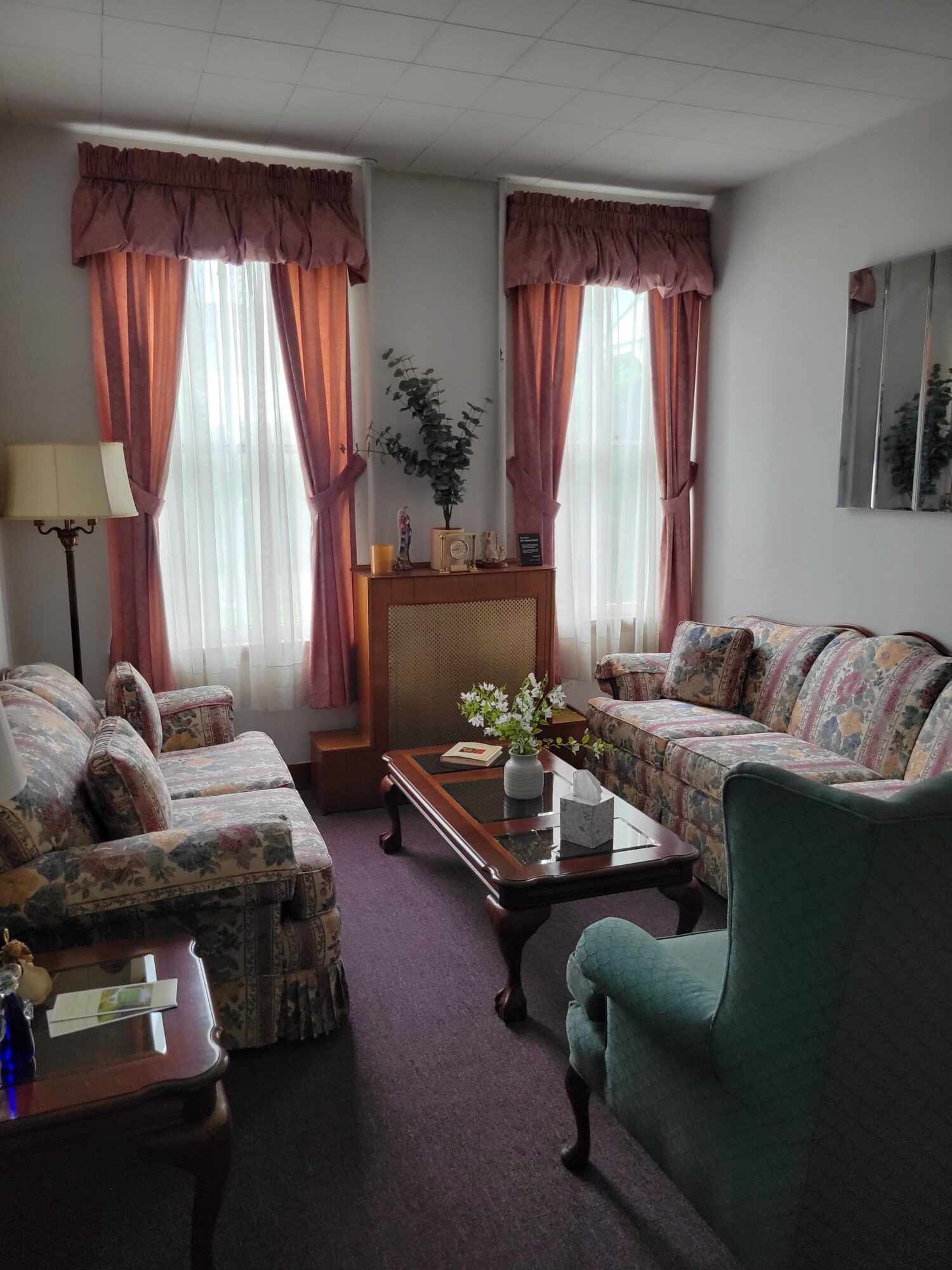 Living room with sofa, armchair, coffee table, and window with curtains, viewed from the side.