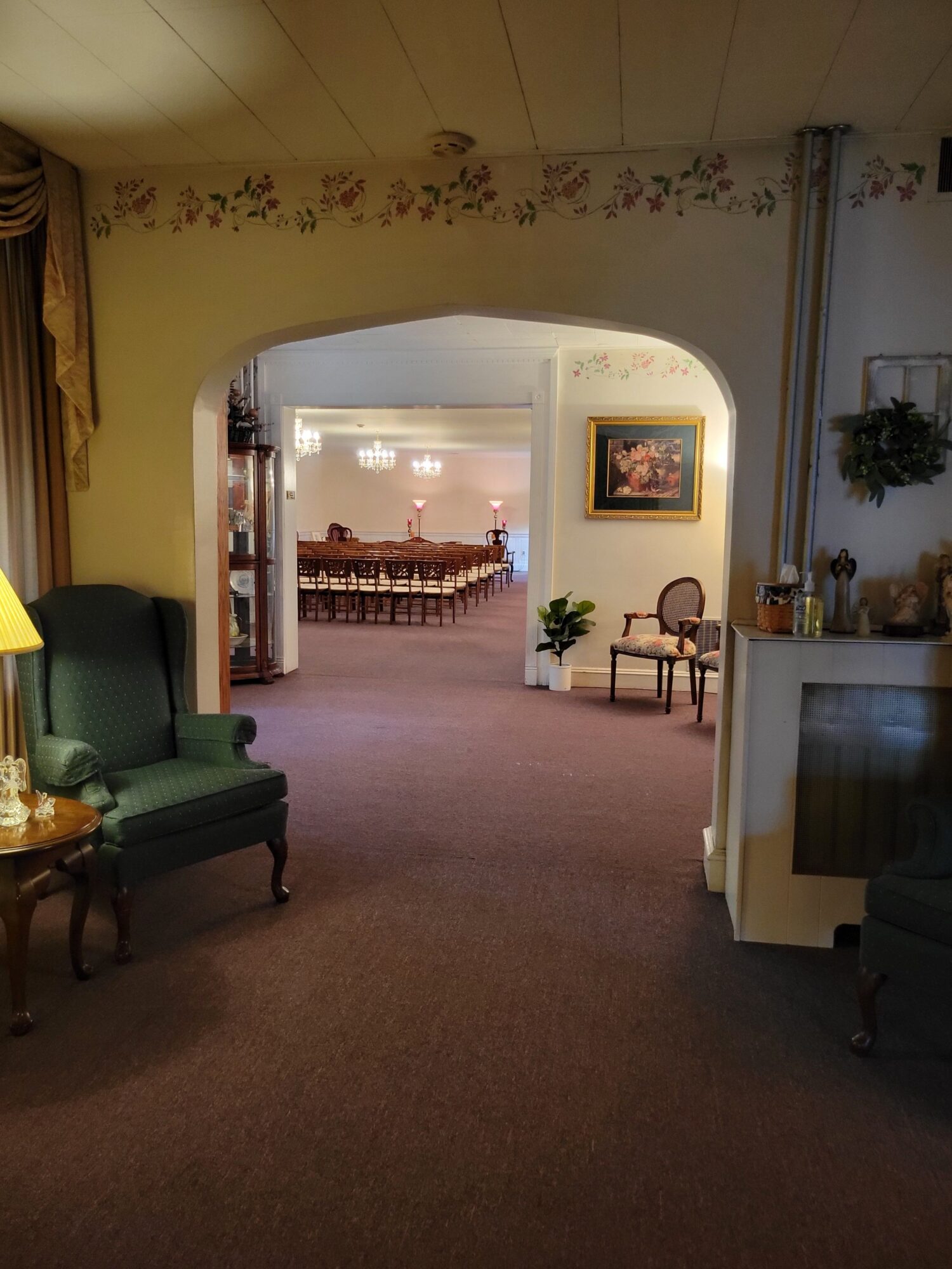 Living room with archway, furniture, and decorations, viewed from the side, with a green armchair in the foreground.