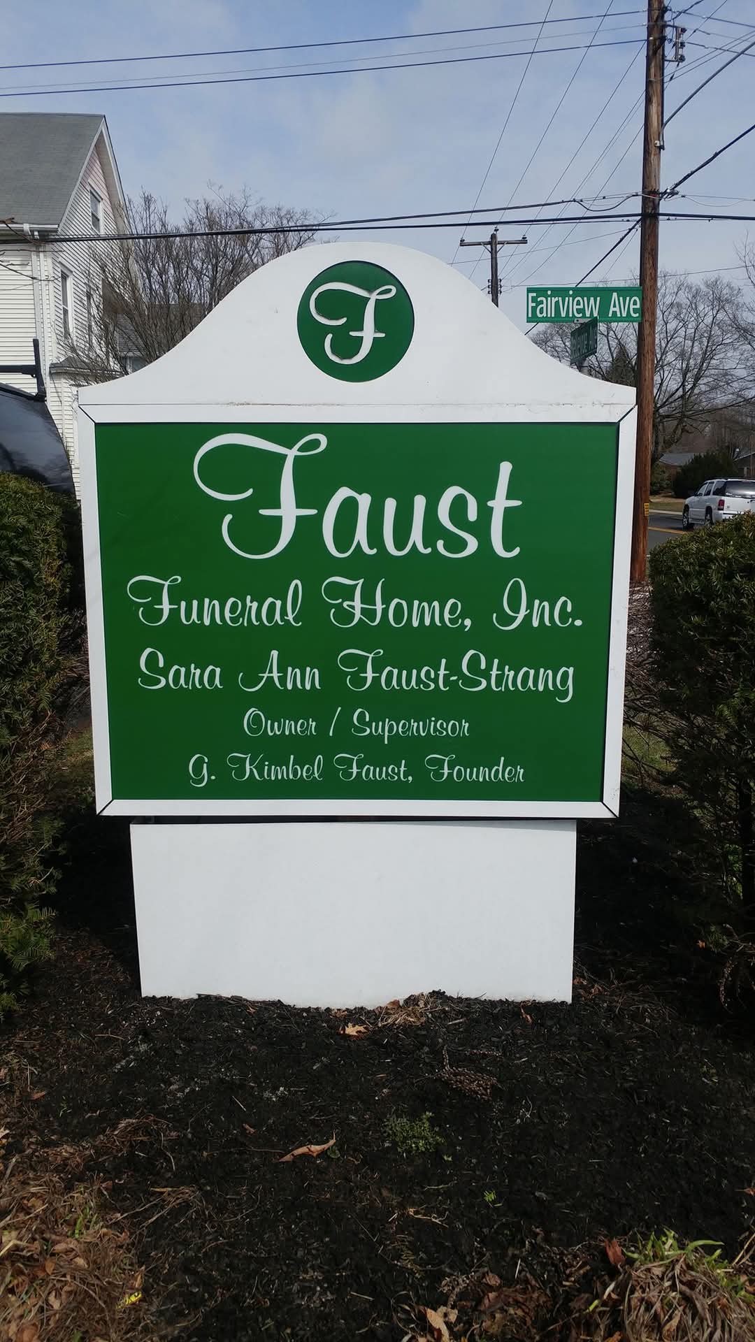 Sign for Faust Funeral Home, Inc., with green and white colors, displaying the business name and services offered.