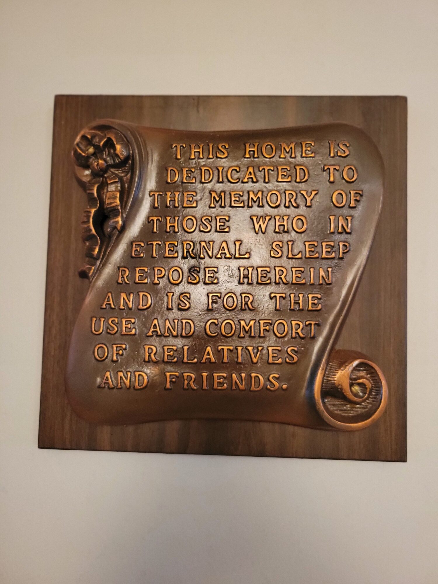 Wooden plaque with engraved text and decorative scroll design, mounted on a wall, with a light background.