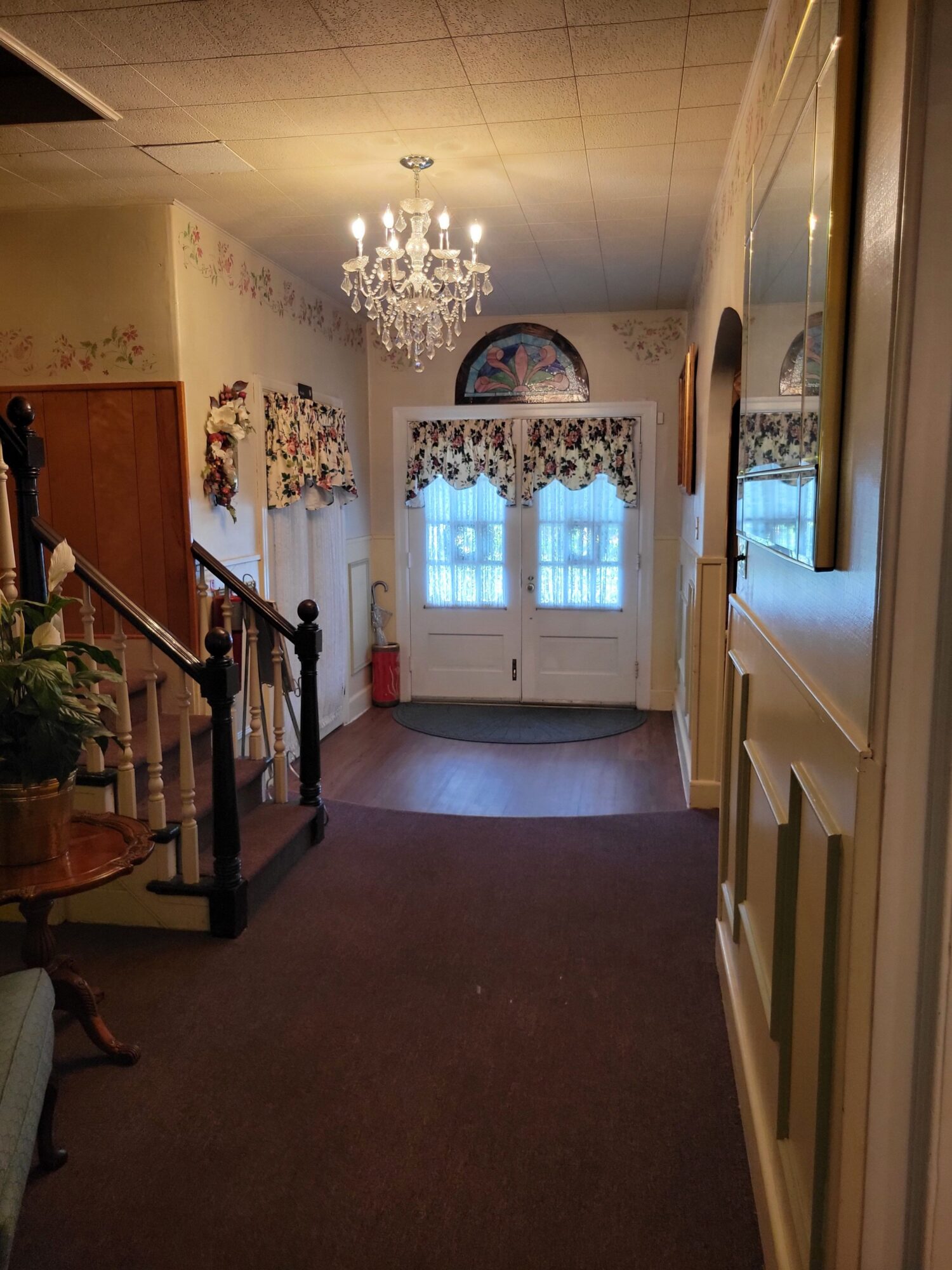 Living room with chandelier, floral curtains, and a window with blue sky view, viewed from doorway.