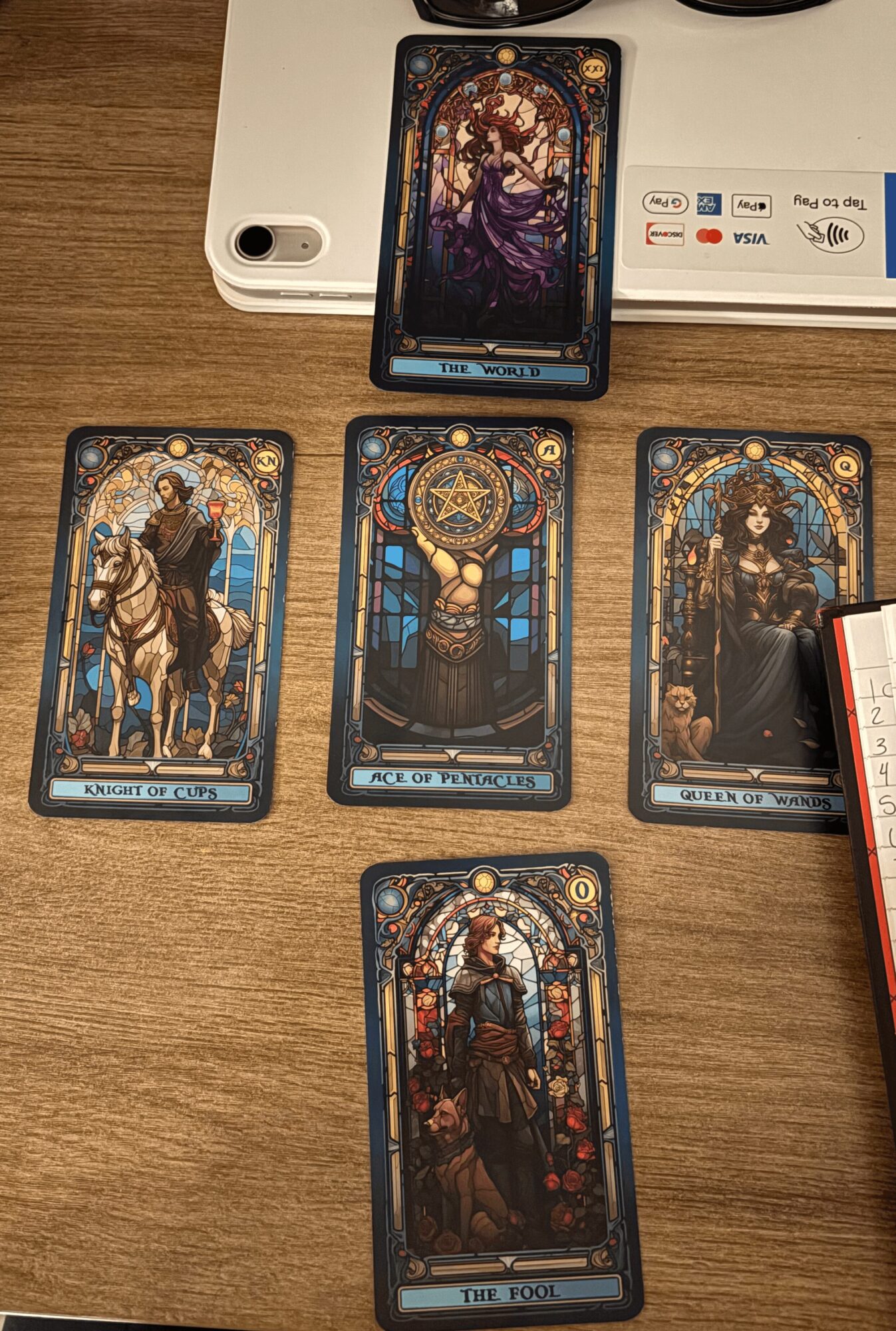 Five tarot cards laid out on a wooden surface, with a smartphone and a white device in the background.