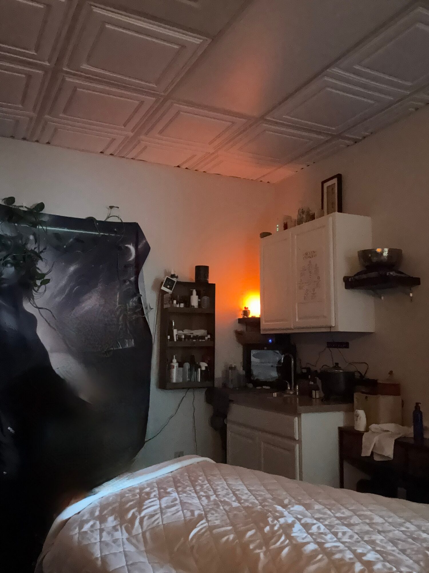 Part of a bedroom with a bed, a white cabinet, shelves, and a ceiling with decorative panels.