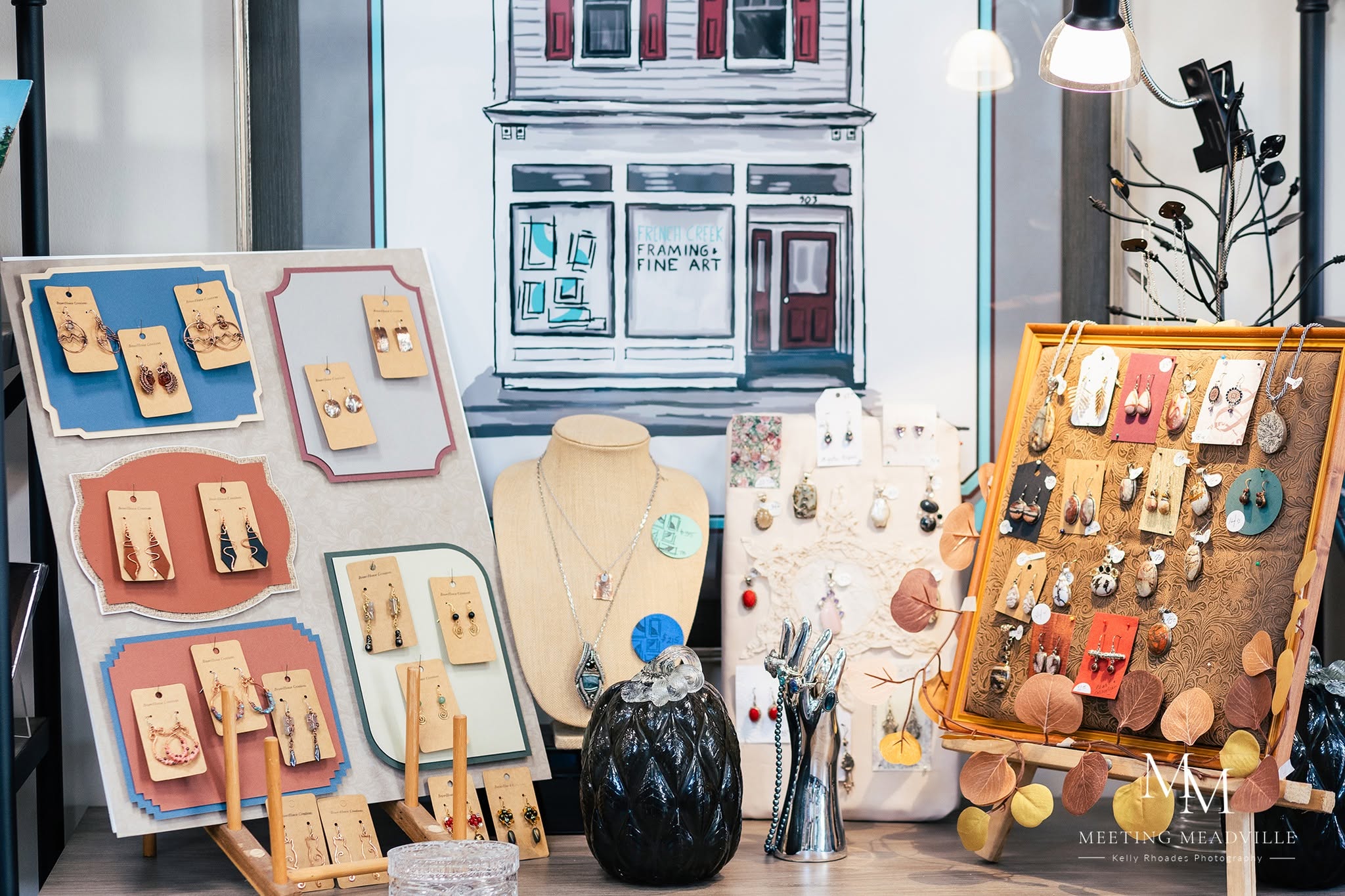 Display of jewelry and accessories on boards and a mannequin in a shop window, with a building visible outside.
