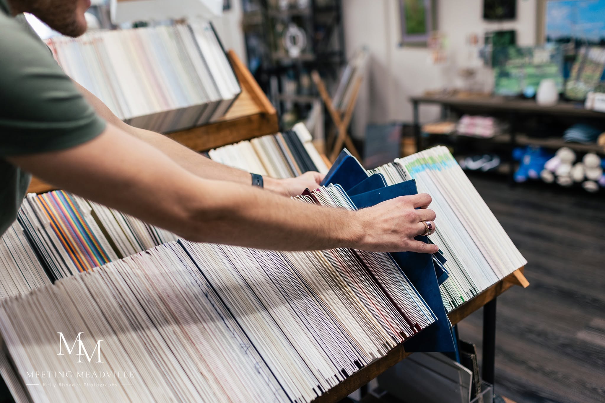 Person browsing color samples in a store, reaching out to select a sample, with shelves of books and supplies in background.