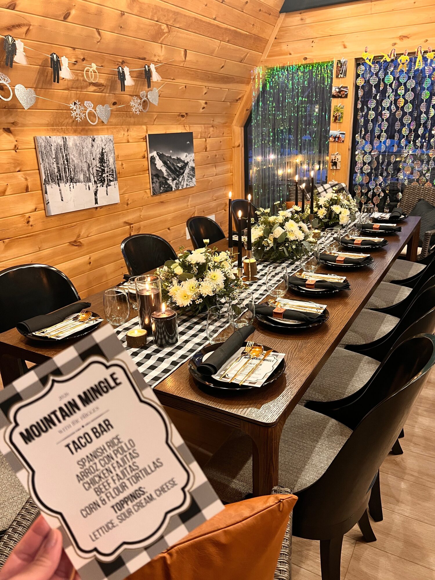 Long dining table set with plates, glasses, and floral centerpieces in a wood-paneled room.