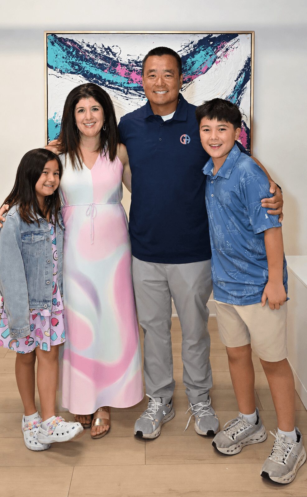 Group of five people standing together indoors, smiling, with a colorful abstract painting behind them.
