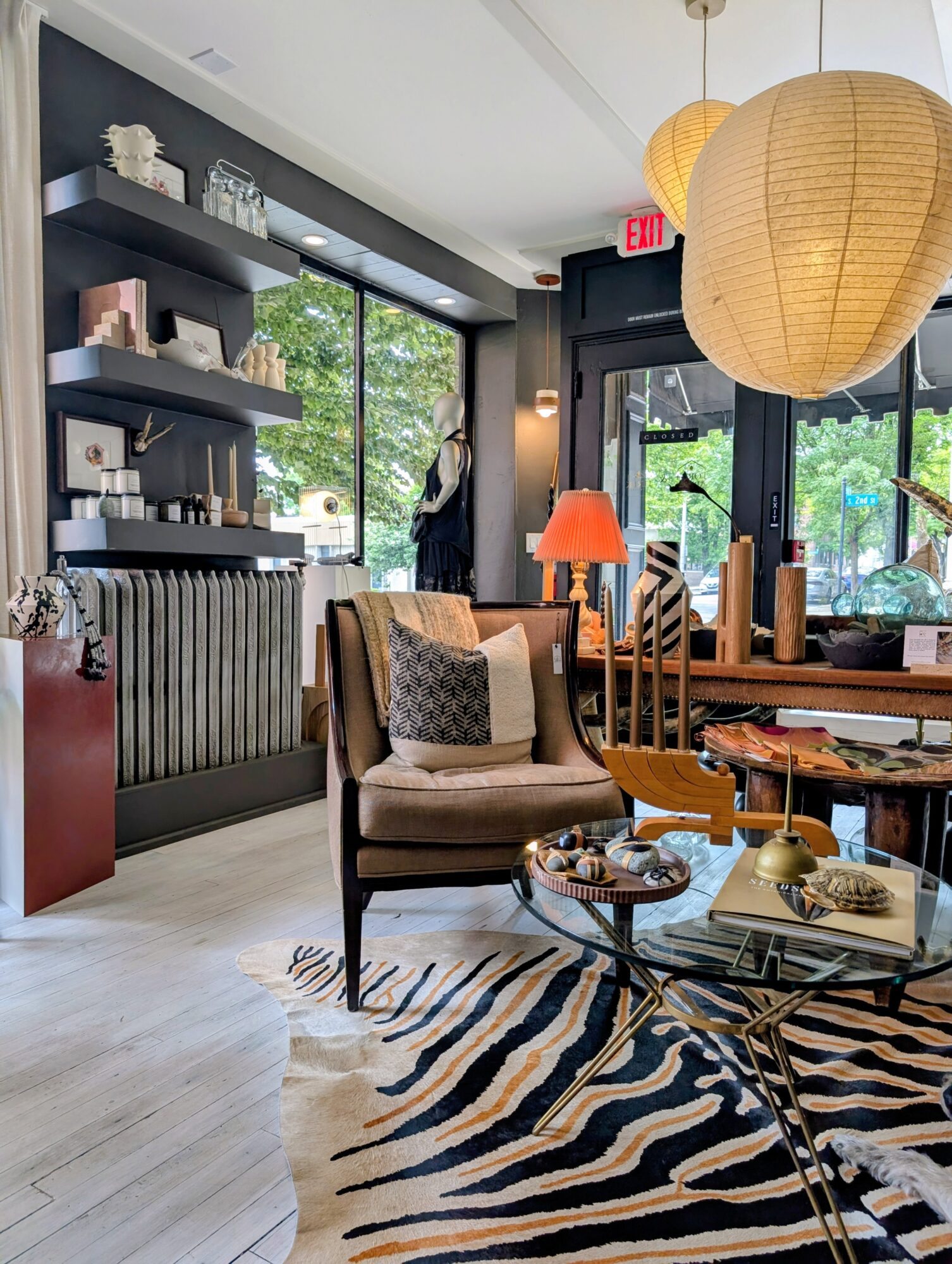 Interior of a cozy cafe with a beige armchair, striped rug, wooden table, and large paper lanterns hanging from the ceiling.
