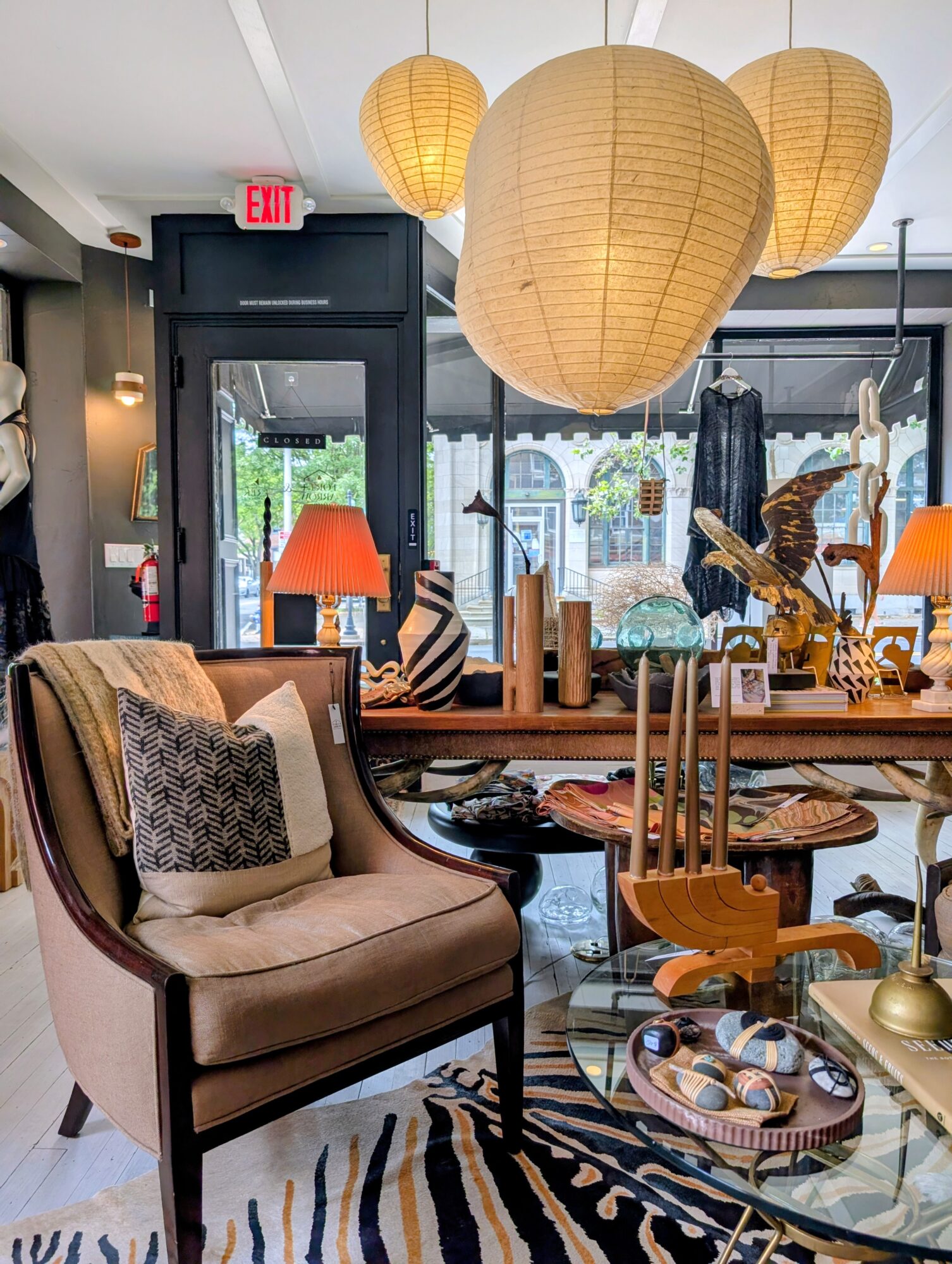 Interior of a cozy room with hanging paper lanterns, a beige armchair with patterned pillows, and a glass coffee table with decorative items.