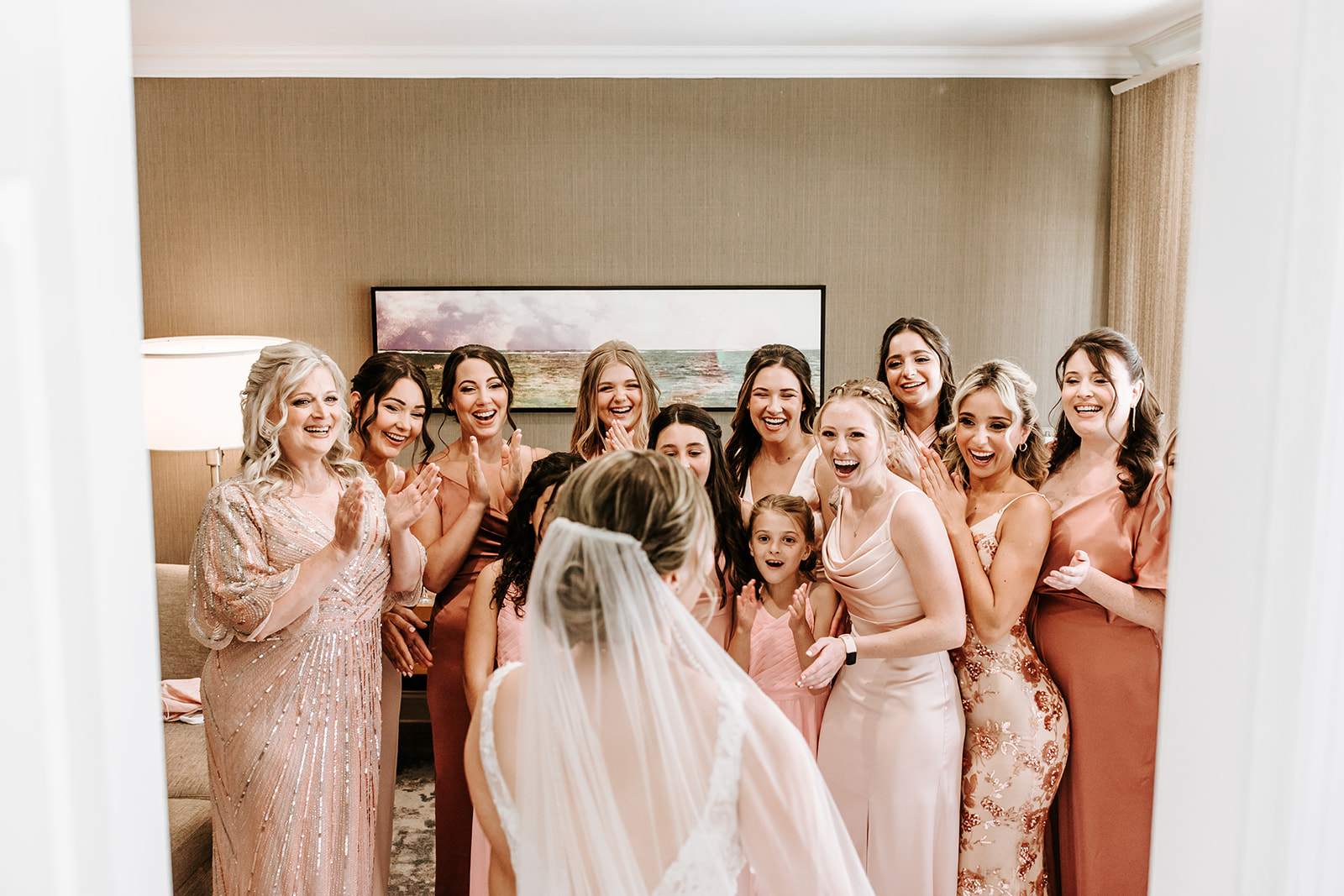 Group of women and girls in a room, celebrating a wedding, with a bride in a veil in the foreground.