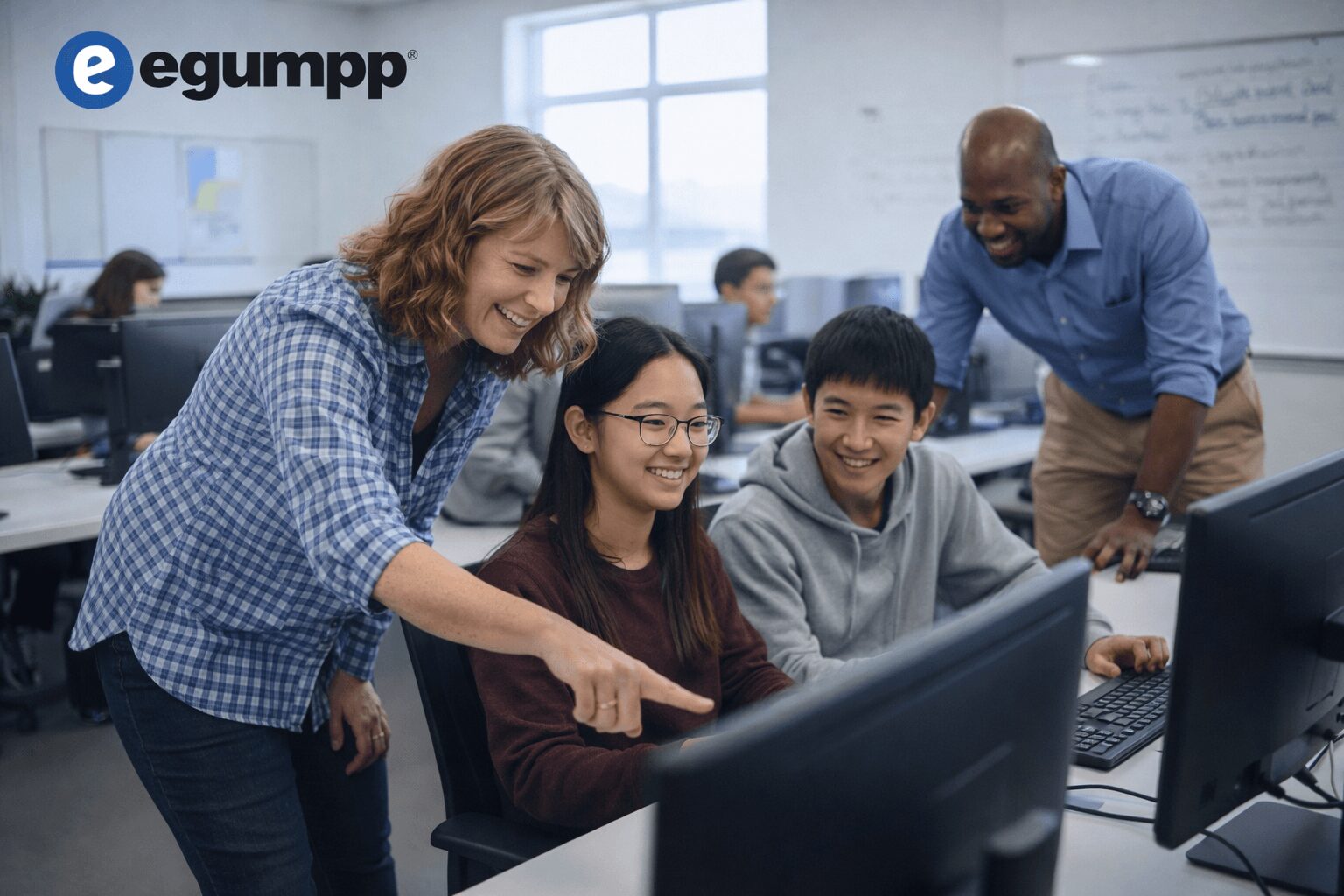 Teacher and students in a classroom working on computers, smiling and engaging with each other.