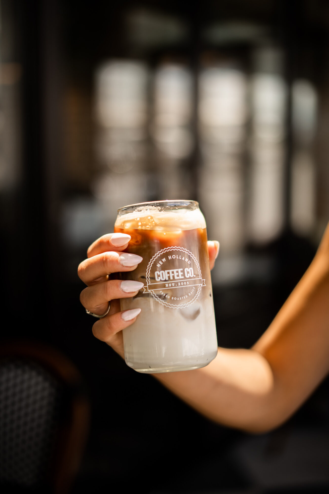 Person holding a glass of iced coffee with a logo, in a dimly lit setting.