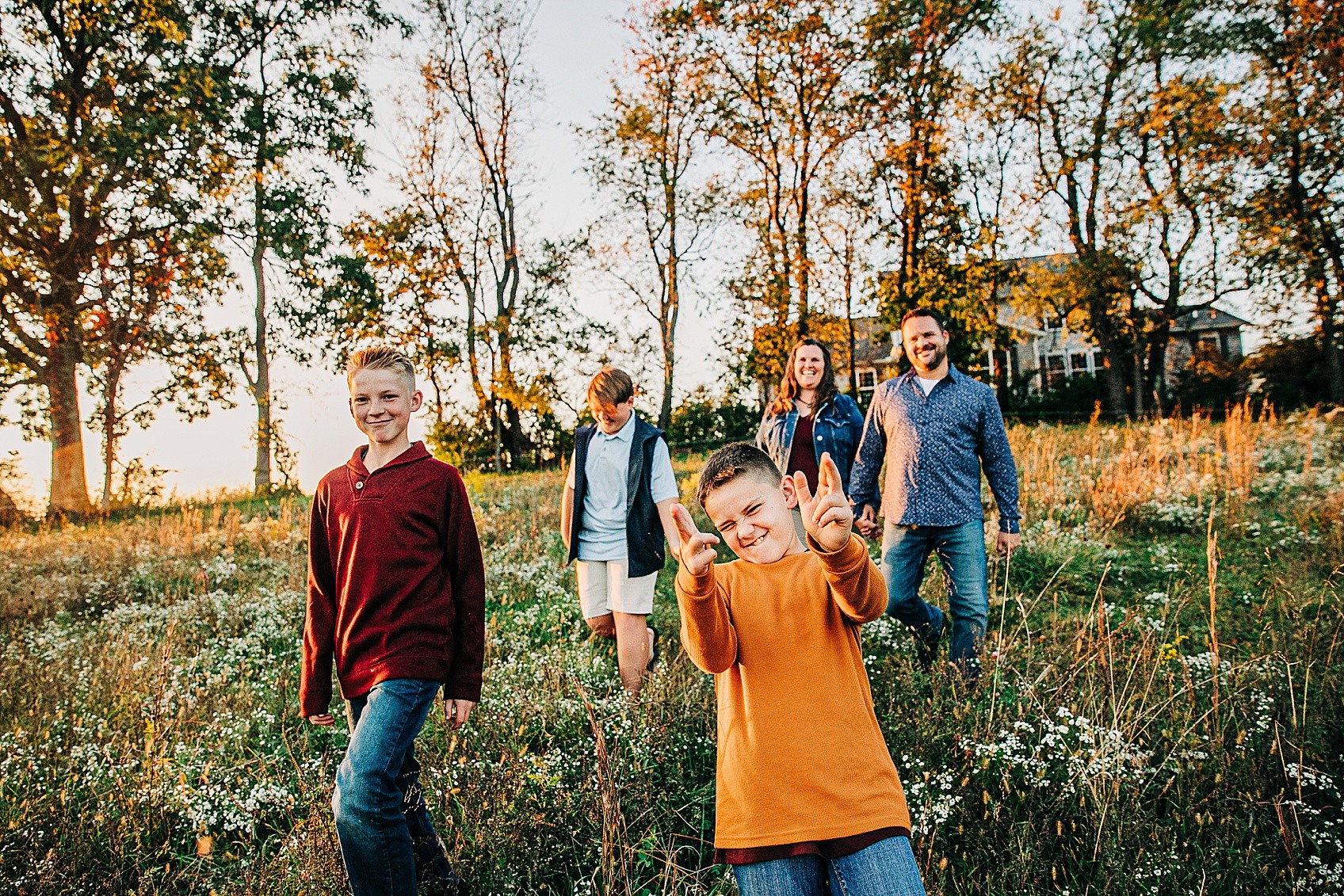 Group of six people walking outdoors in a field with trees and a house in the background, smiling and enjoying the day.