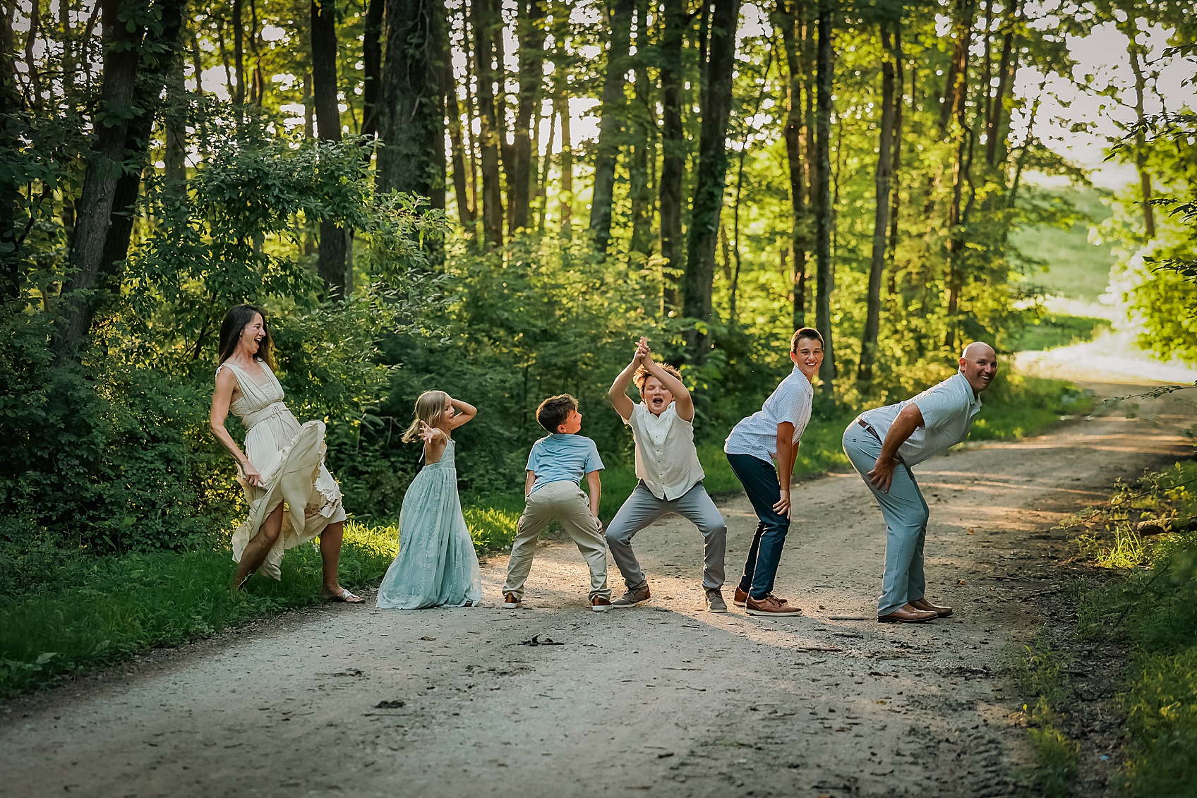 Group of people, including children, standing on a dirt path in a forested area with sunlight filtering through trees