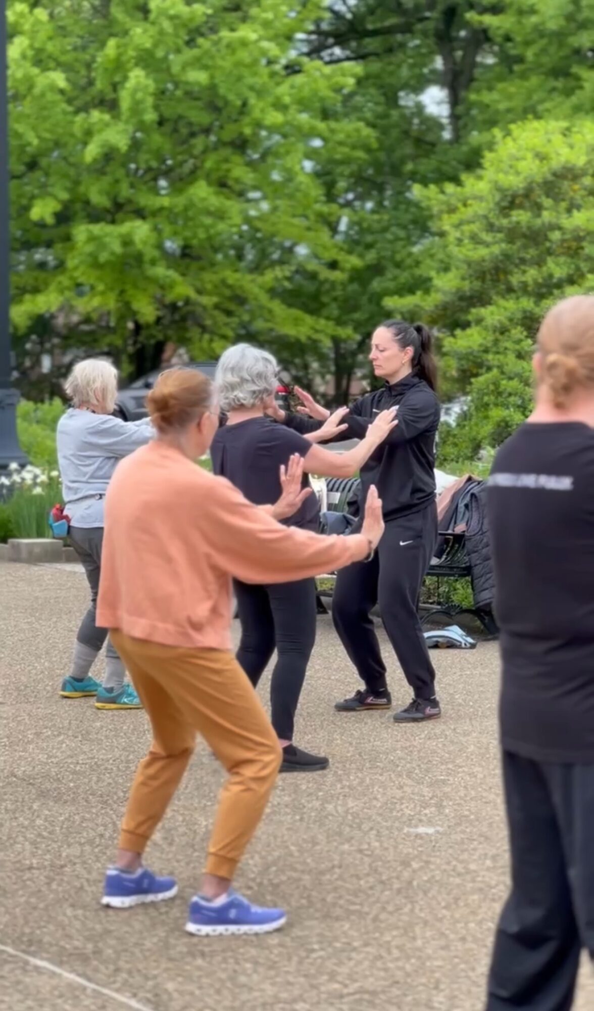 Group of people dancing outdoors on a paved area with green trees in the background.