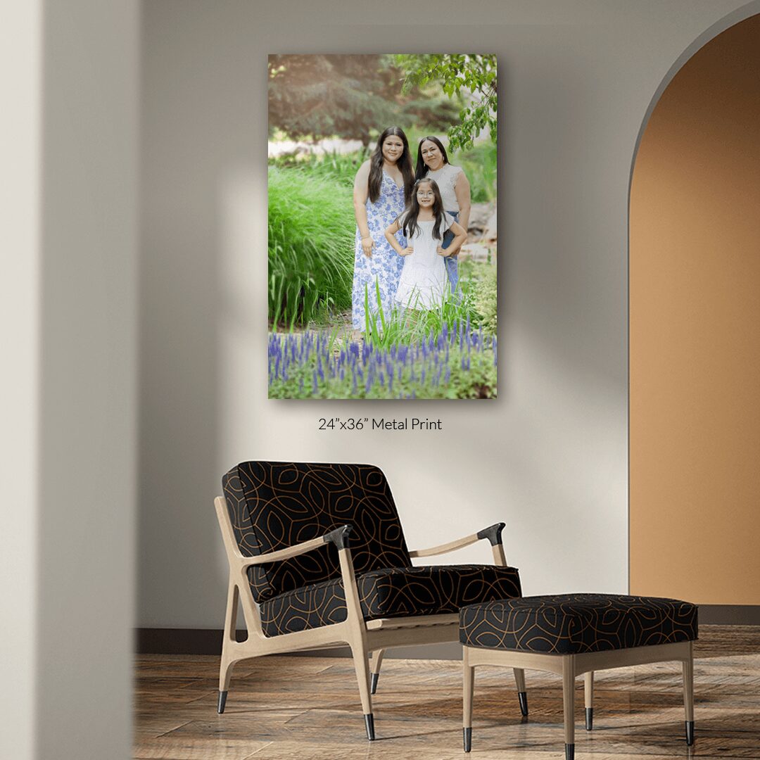 Framed photo of three women outdoors with greenery and purple flowers, hanging on a wall above a black armchair and ottoman.