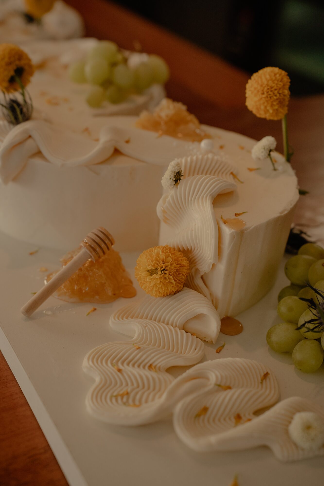 Close-up of a decorated cake with cream, honeycomb, and floral decorations, with grapes nearby.