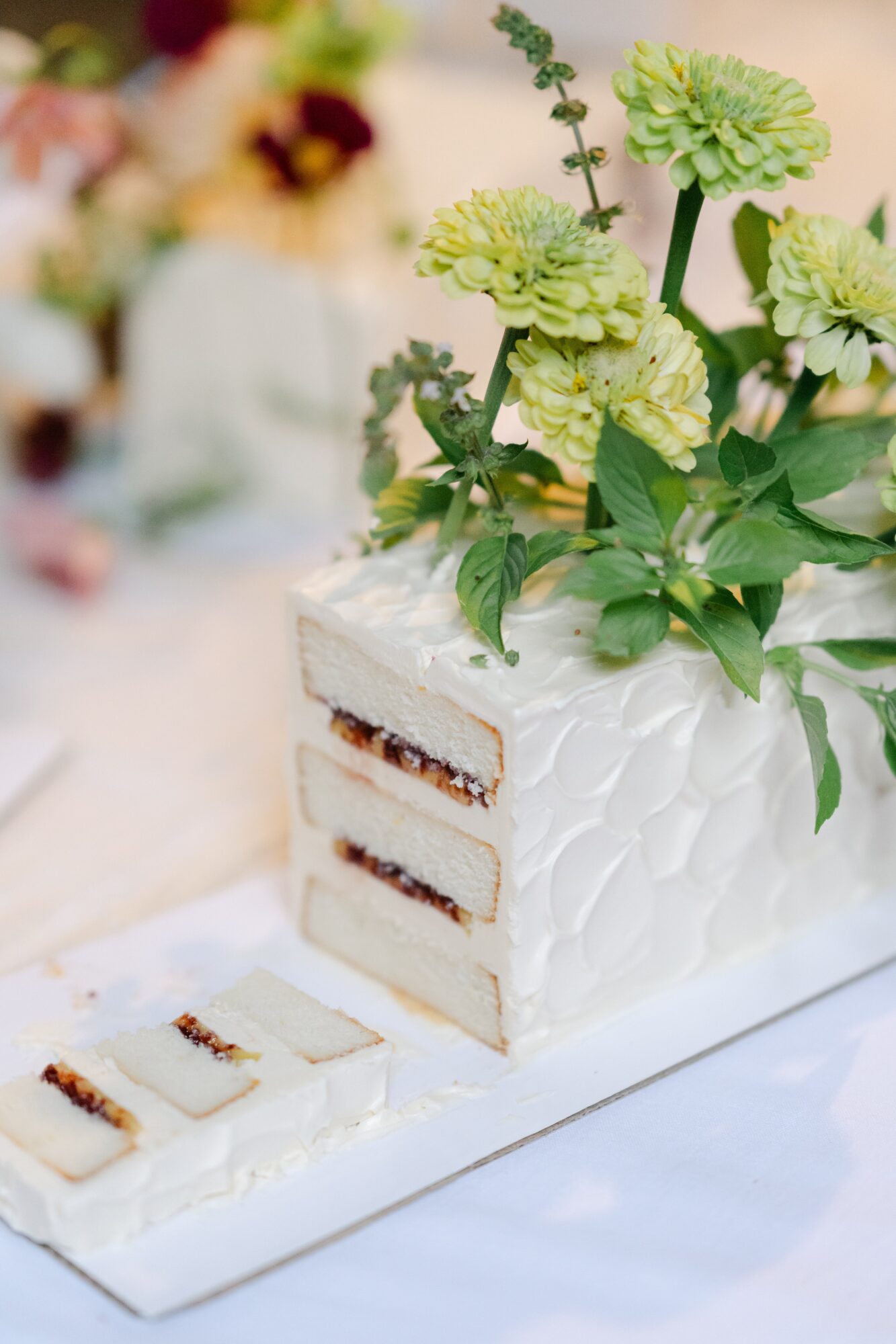 A white cake with textured icing, decorated with green flowers and leaves, partially sliced to show layers inside.