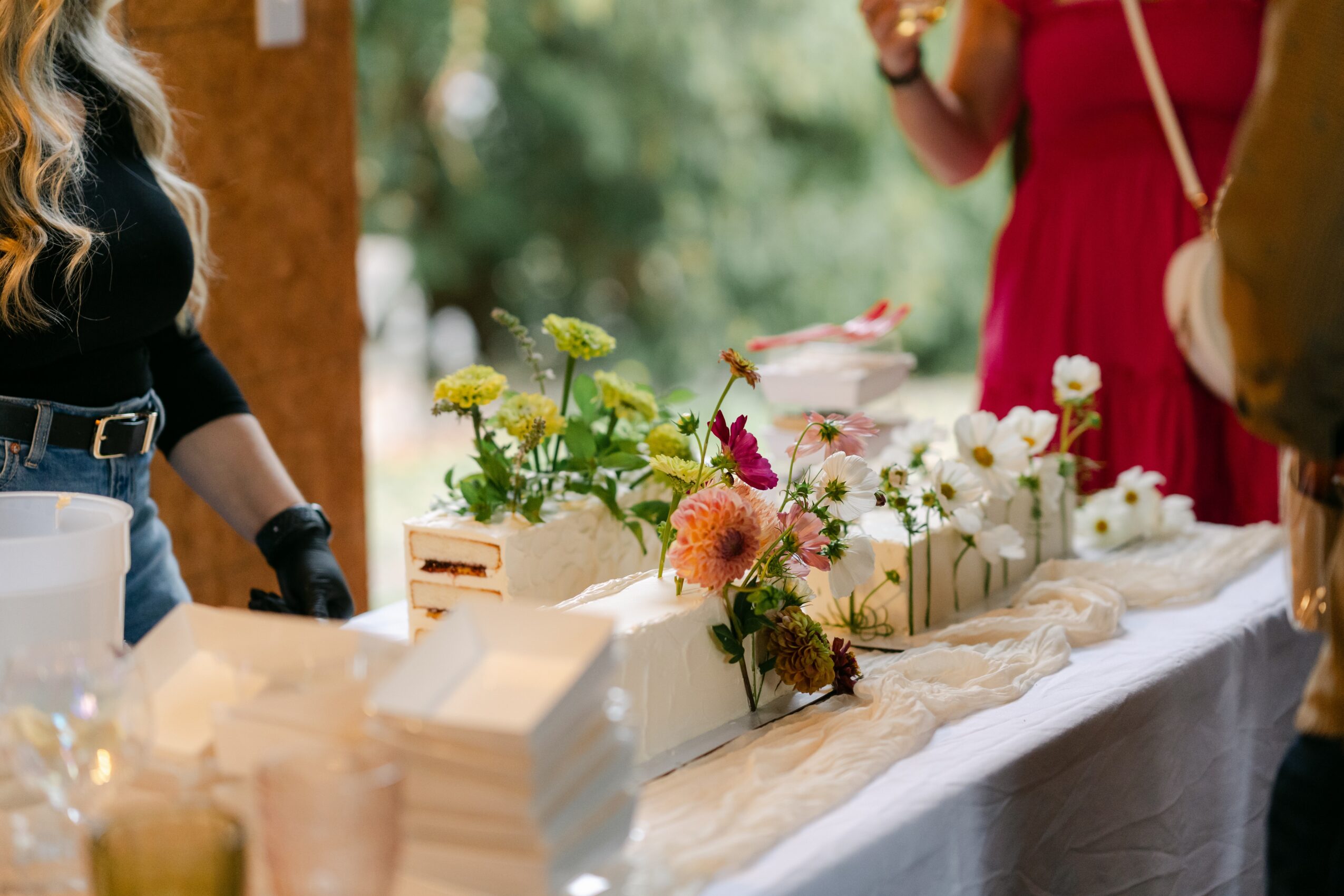 Flowers arranged on a table with people around, outdoors setting, blurred background, natural light.