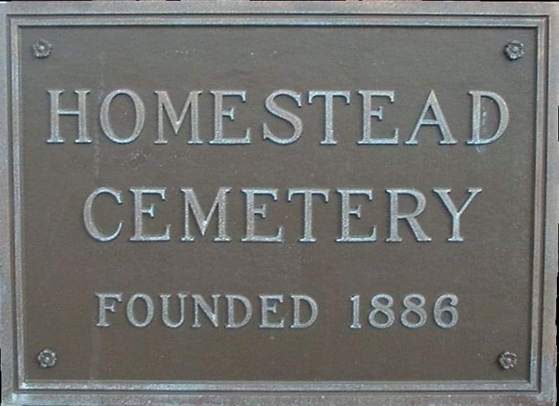 Metal sign reading 'HOMESTEAD CEMETERY FOUNDED 1886' with embossed letters.