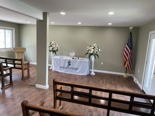 Room with a table decorated with flowers, an American flag, and a window, with wooden flooring and seating area.