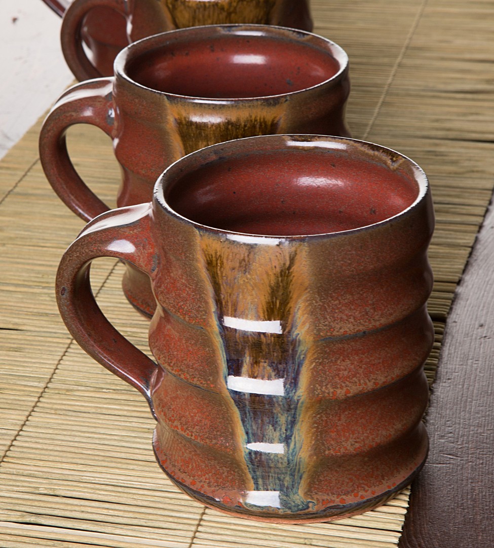 Two ceramic mugs filled with a dark liquid on a wooden surface, with a woven mat nearby.