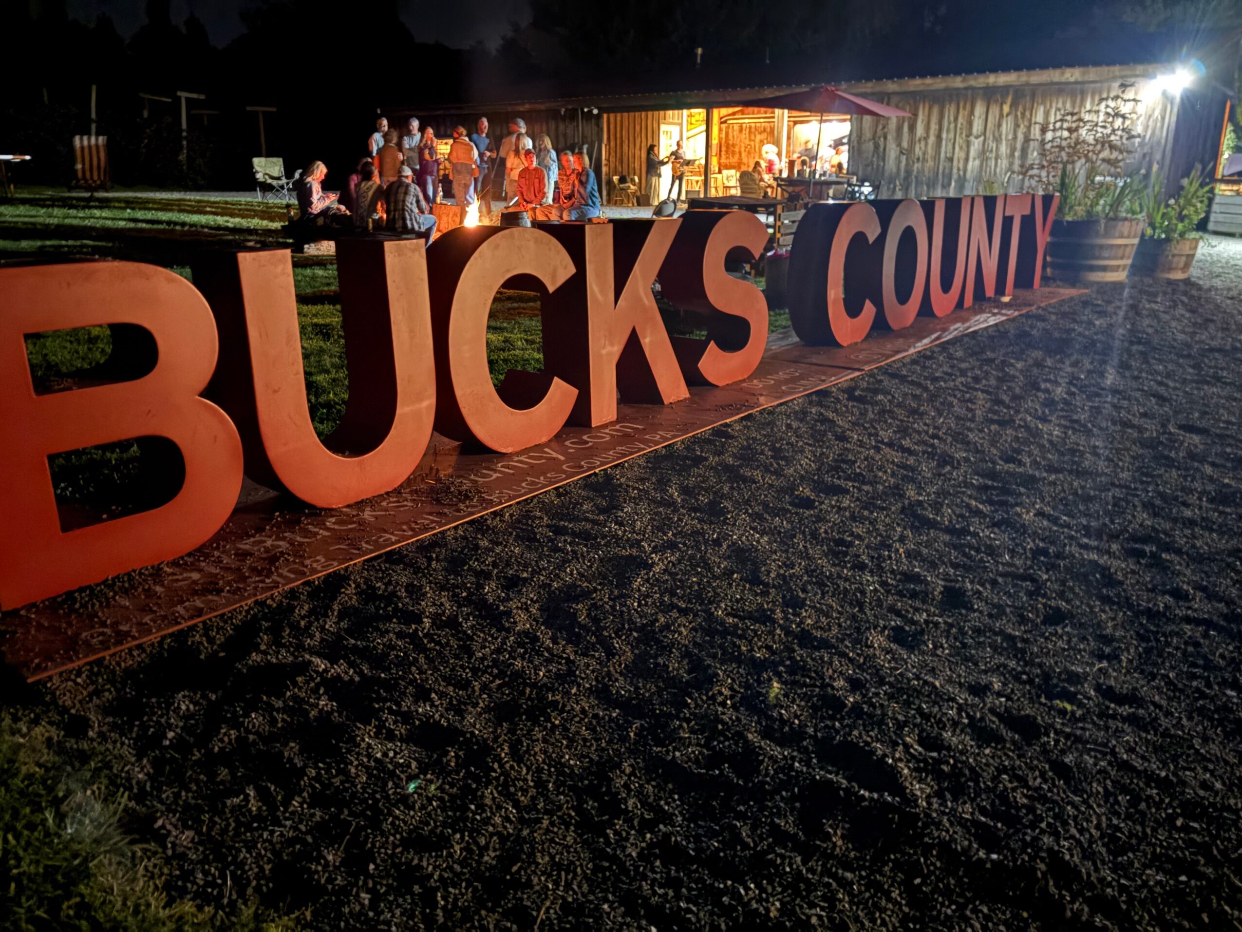 Large illuminated sign spelling BUCKS COUNT with people gathered in the background at night.