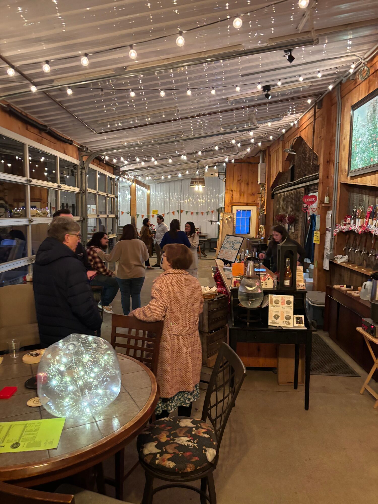 People gather inside a cozy wooden cafe with string lights, a globe, and a counter area, seen from above.