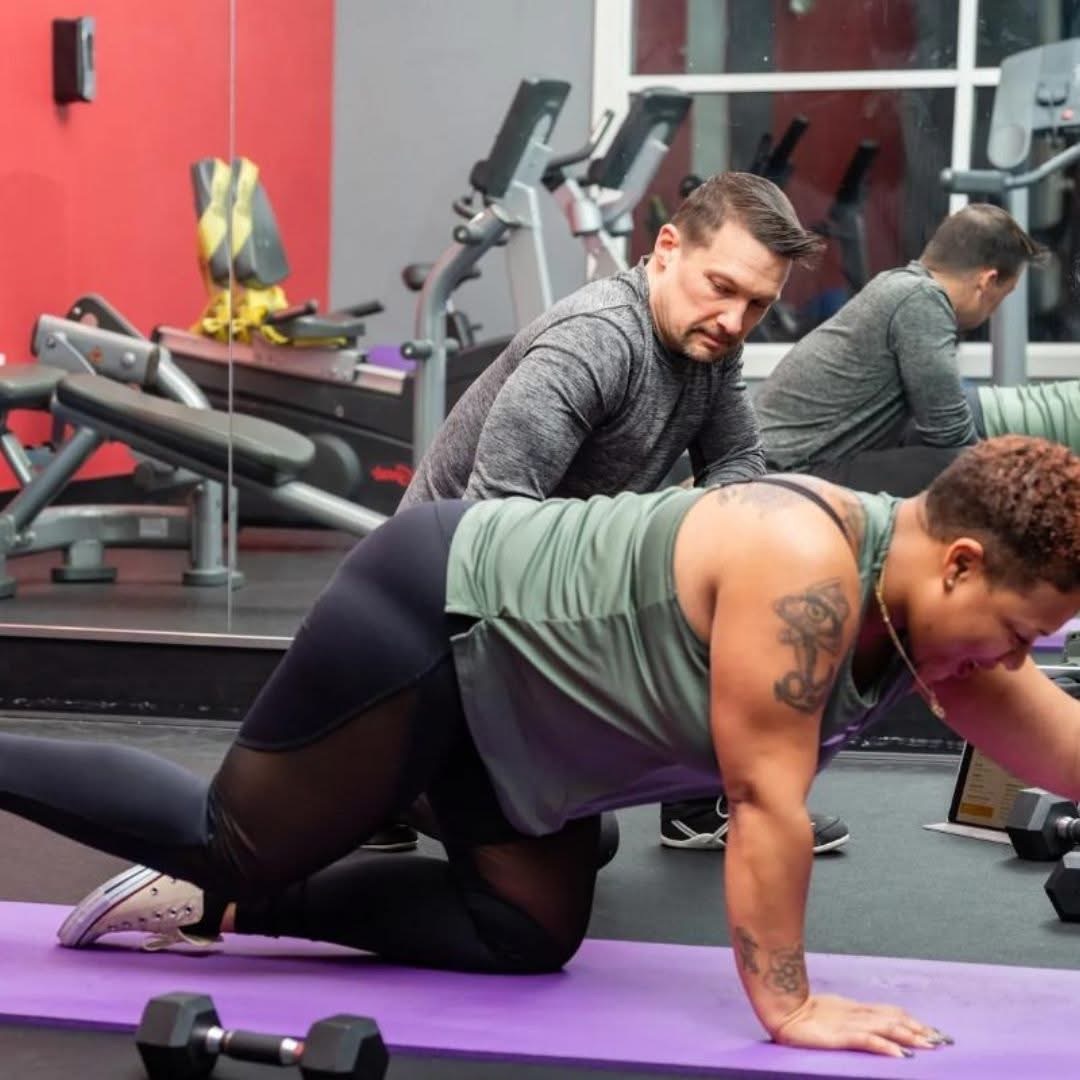 Two men exercising on a purple yoga mat in a gym, with gym equipment in the background.
