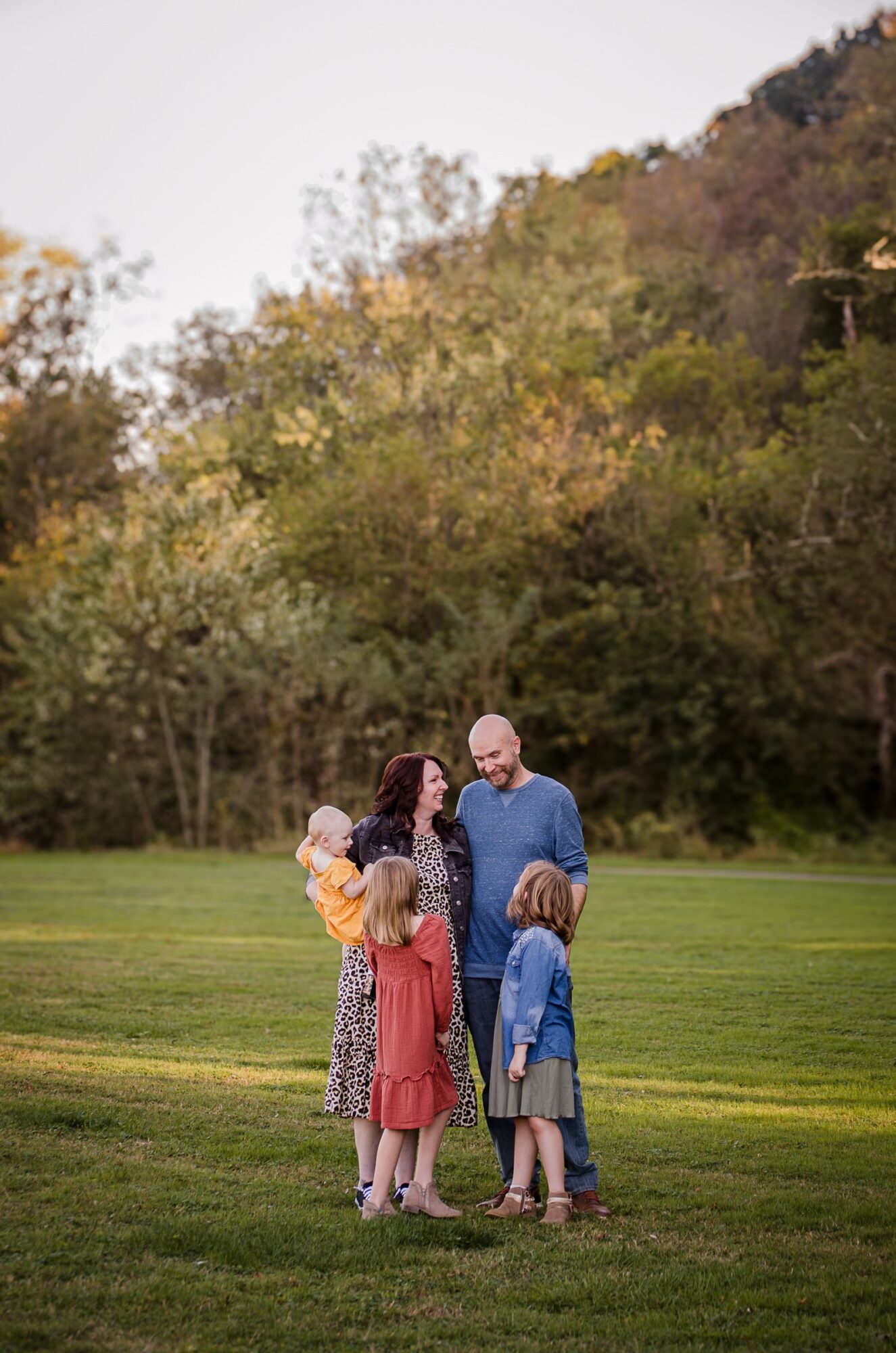 Family of five standing on grass in a park with trees in the background, talking and smiling.