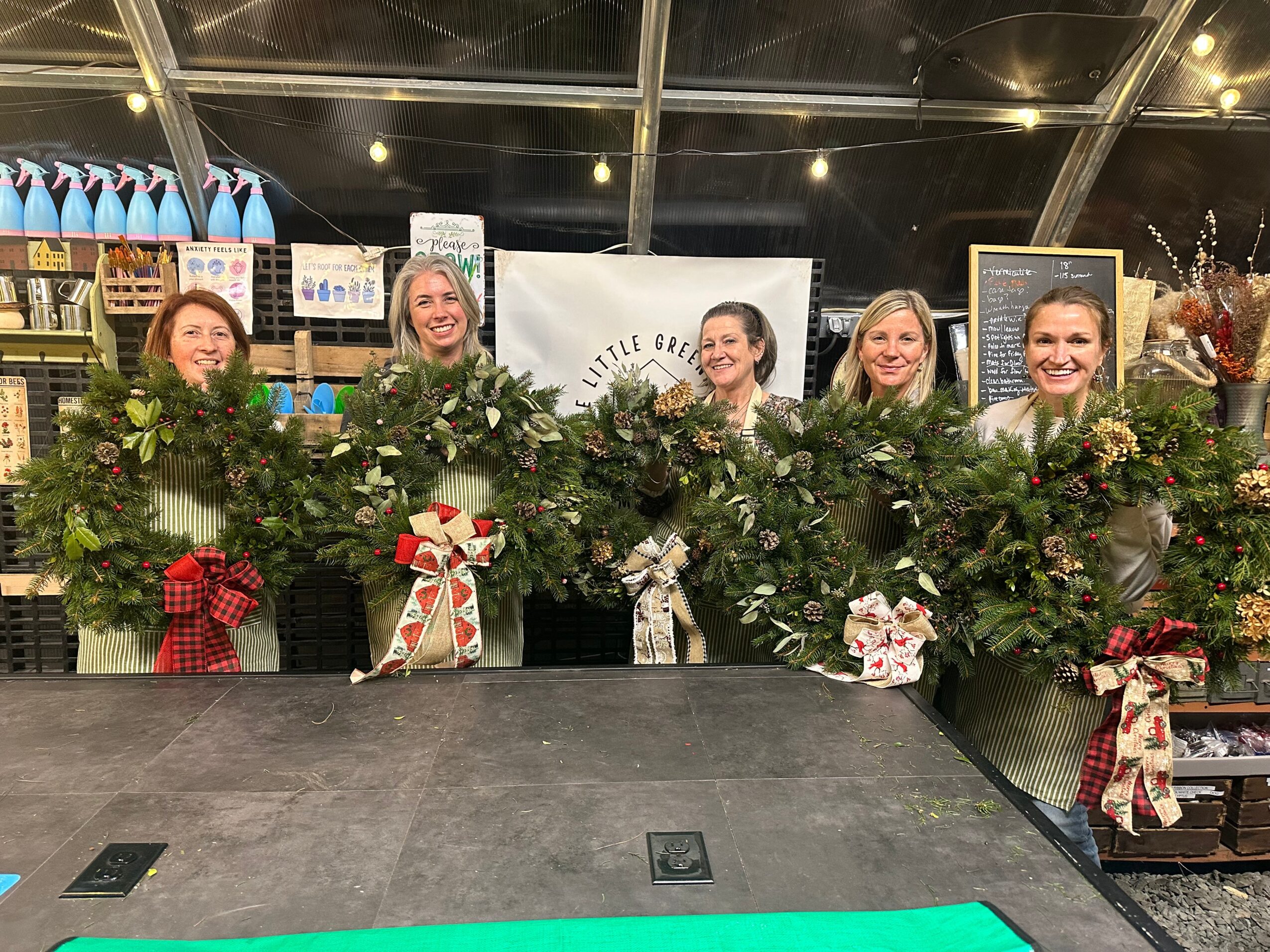 Five women stand behind a decorated table with greenery and flowers, smiling at the camera, in a store setting.