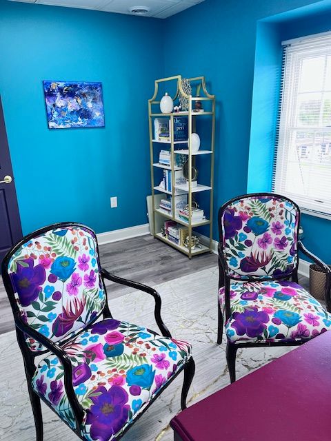 Room with blue walls, a white bookshelf, floral chairs, and a small painting on the wall.