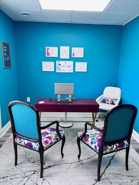 Blue wall with framed pictures, desk with a computer monitor, and two chairs with floral cushions.