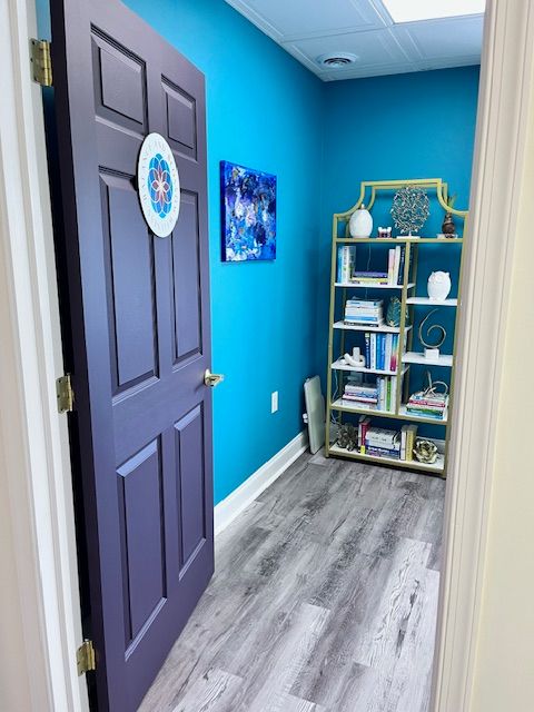 Room with blue wall, bookshelf, and gray flooring, viewed through a partially open dark purple door.