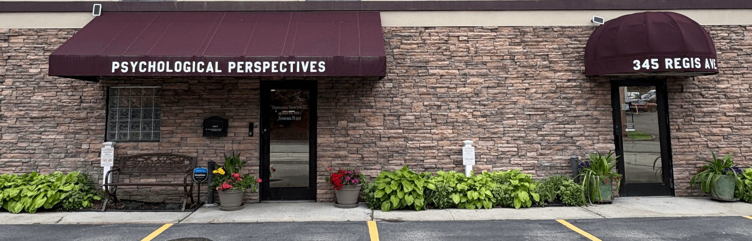 Storefront with a sign reading 'Psychological Perspectives' and a brick exterior, with plants and a bench outside.
