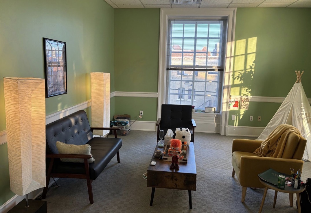 Room with green walls, large window, black and yellow chairs, a teepee, and a table with toys.