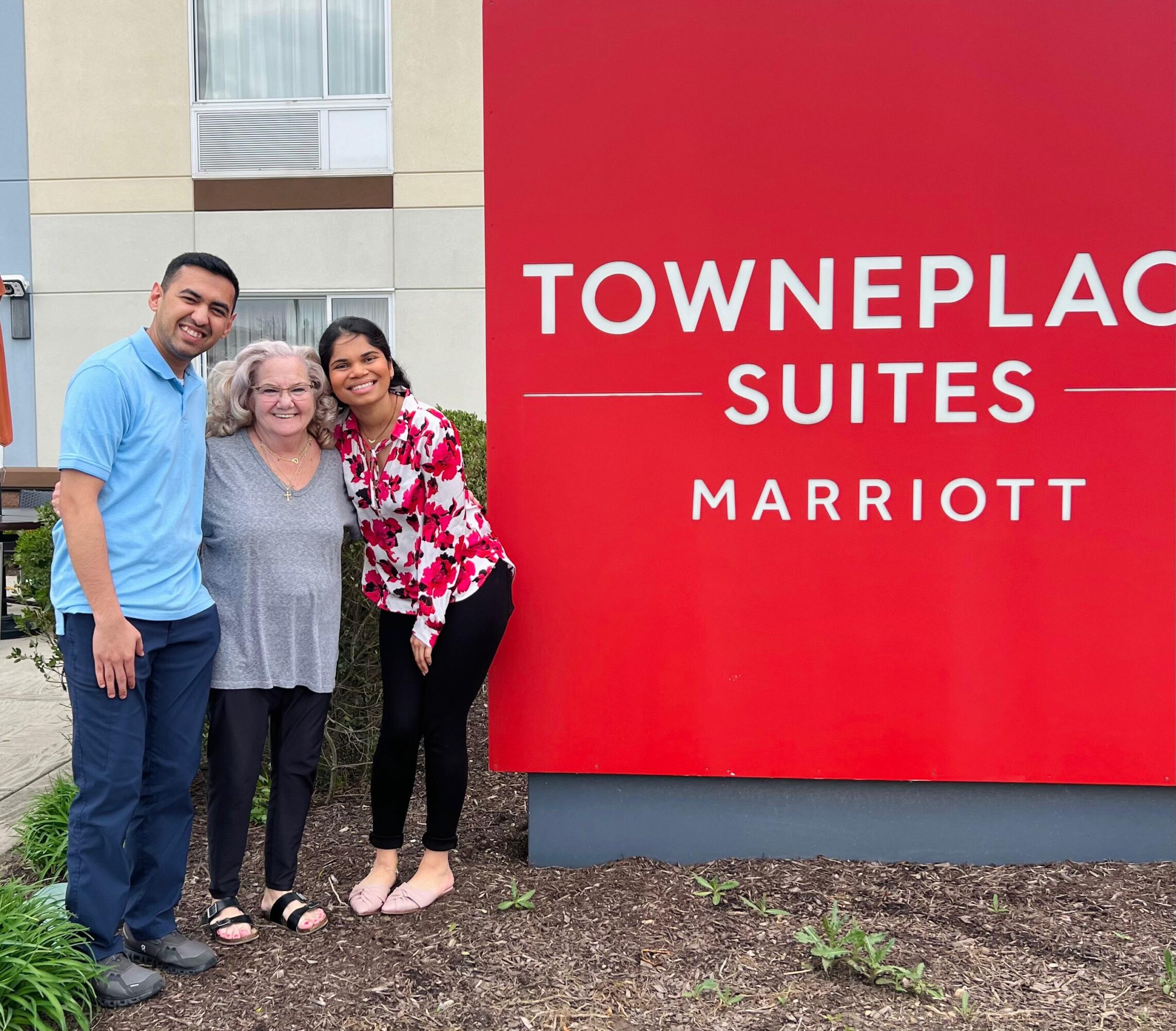 Four people standing outside near a red sign that reads 'TOWNEPLACE SUITES MARRIOTT'.