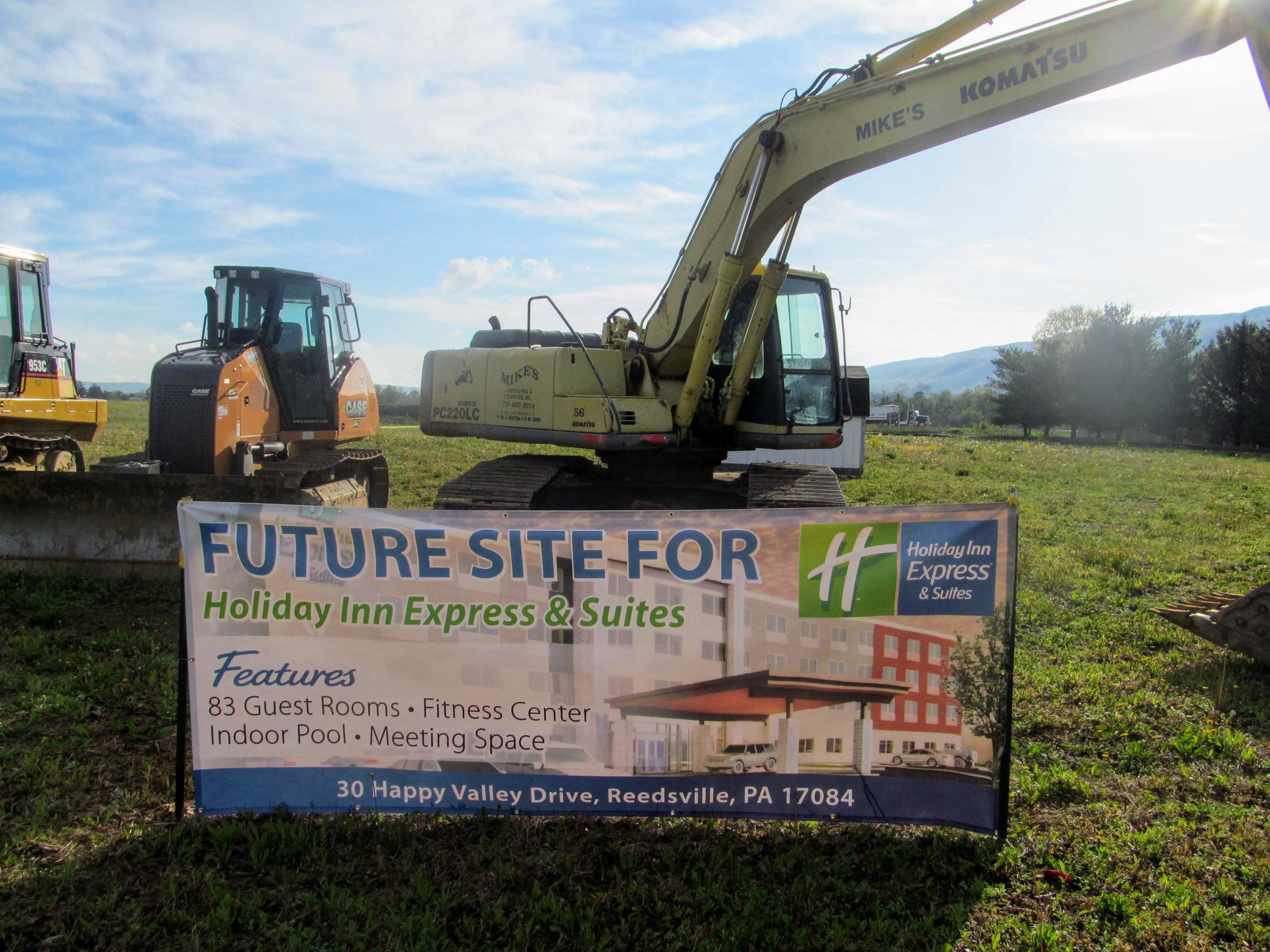 Construction site with excavator and a sign for future development, blue sky, and open field background.