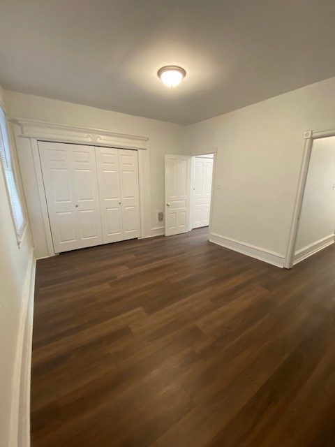 Empty room with white walls, hardwood floor, closet, door, and window, illuminated by ceiling light.