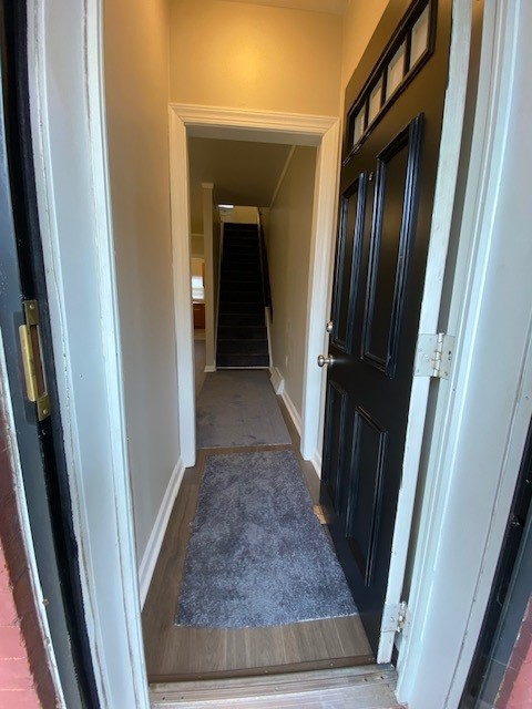 Narrow hallway with a black door on the right, carpeted floor, and stairs visible at the end.