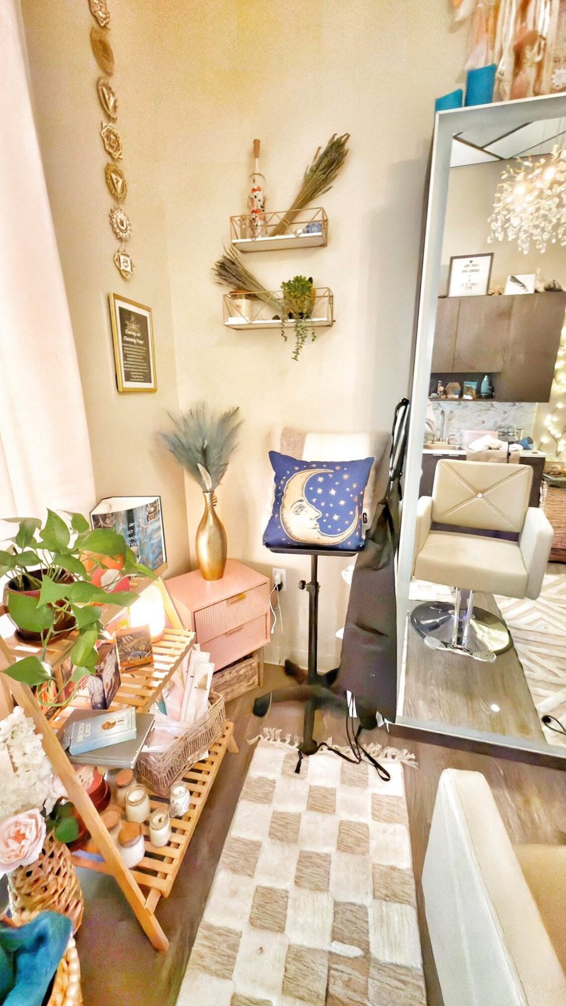 Living room corner with a pink side table, plants, a chair with a blue cushion, and a mirror reflecting part of the room.
