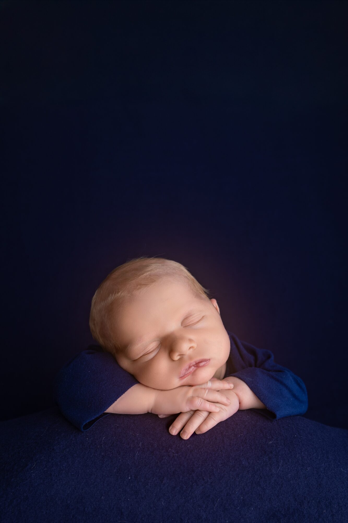 Young child with closed eyes resting head on hands, against dark background.