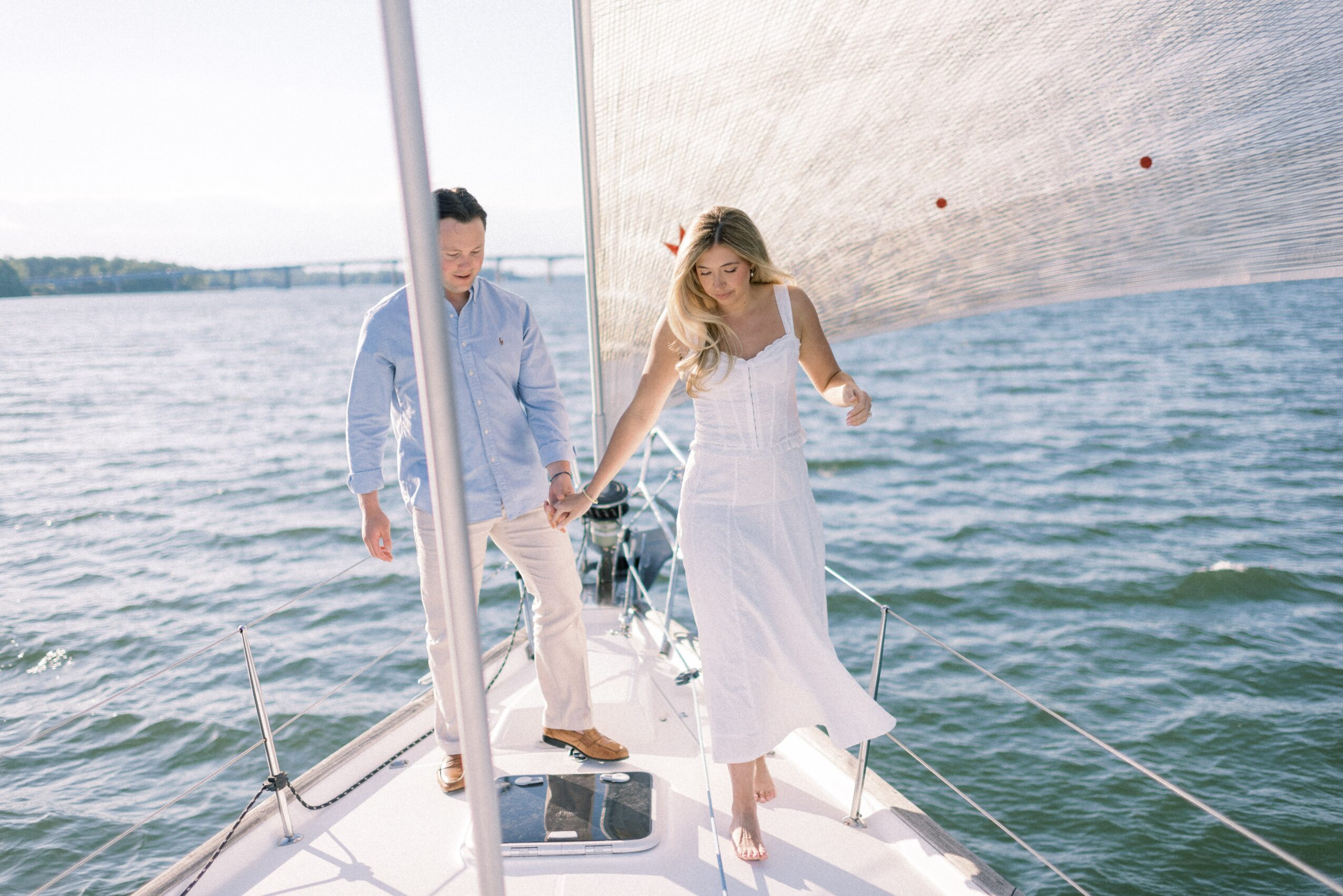 A couple on a sailboat holding hands, with water and a city skyline in the background.